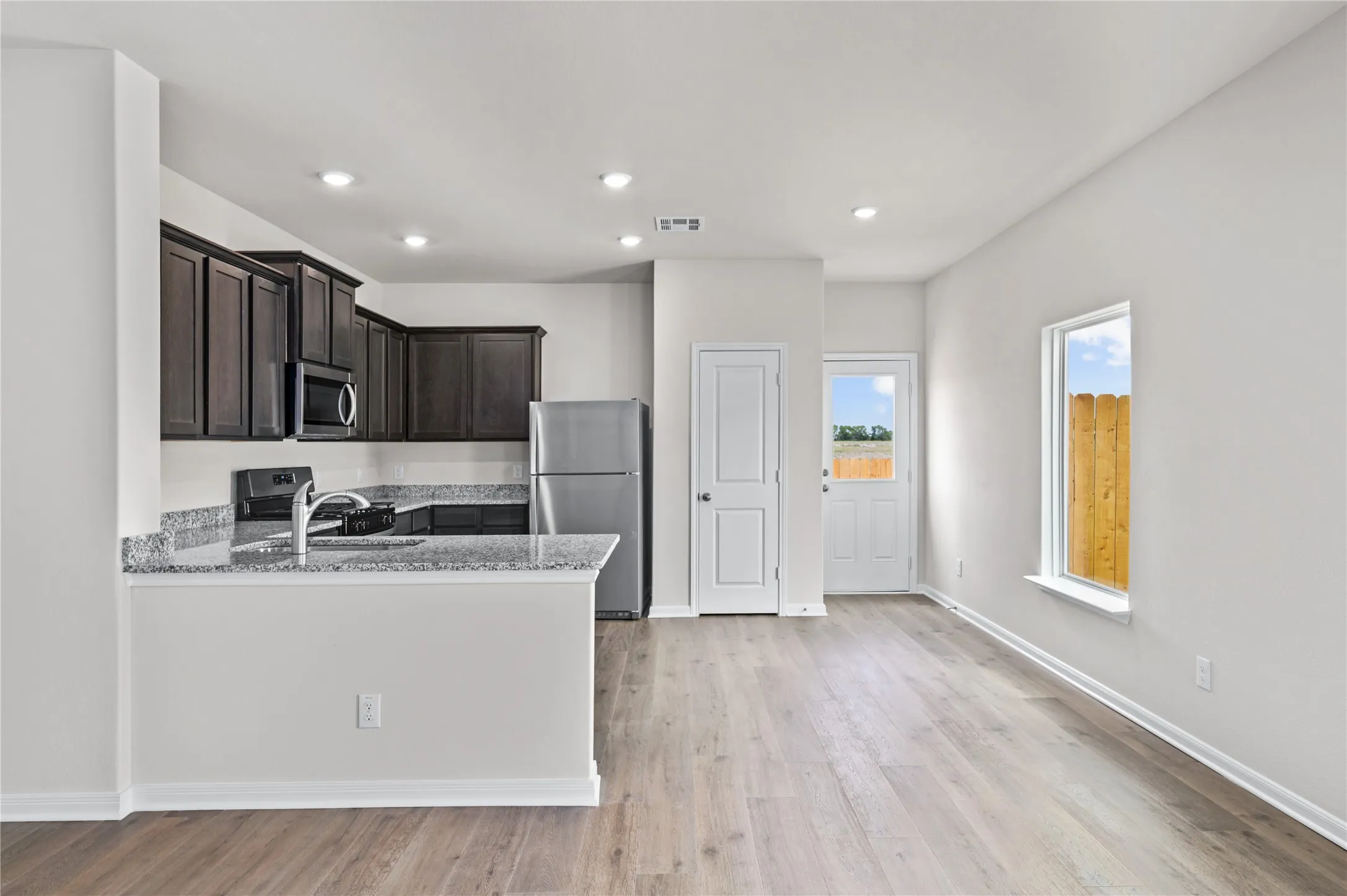 Kitchen with light stone countertops, stainless steel appliances, light wood-style flooring, recessed lighting, and a peninsula