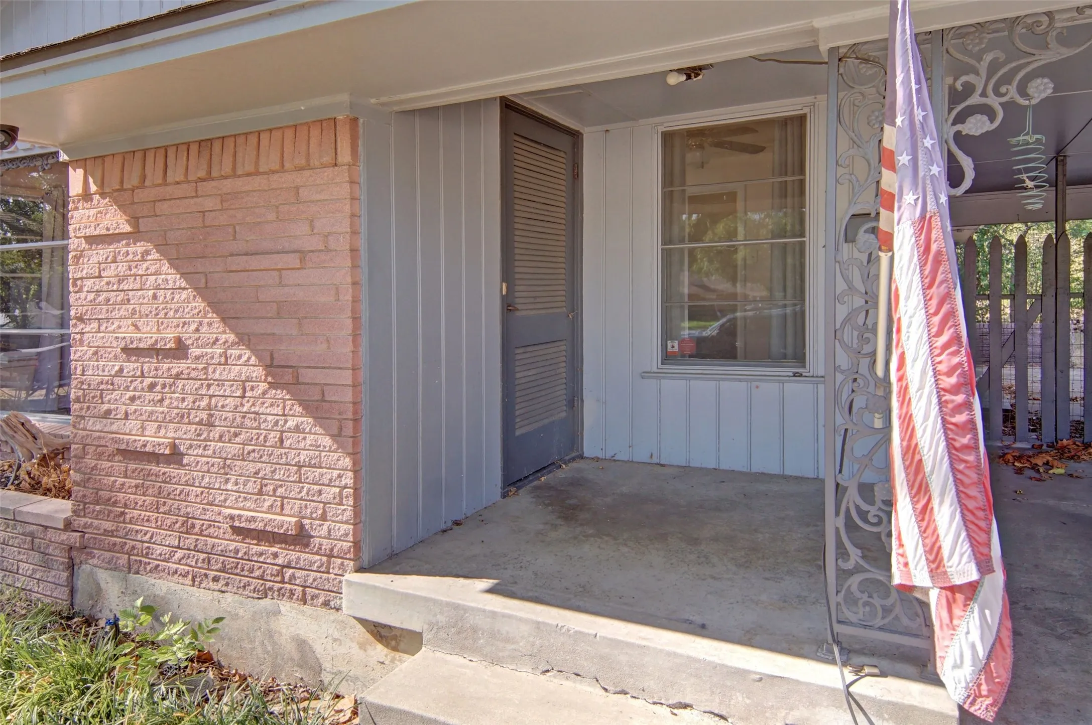 Brick facade with vertical siding, covered concrete porch, and decorative wrought iron column