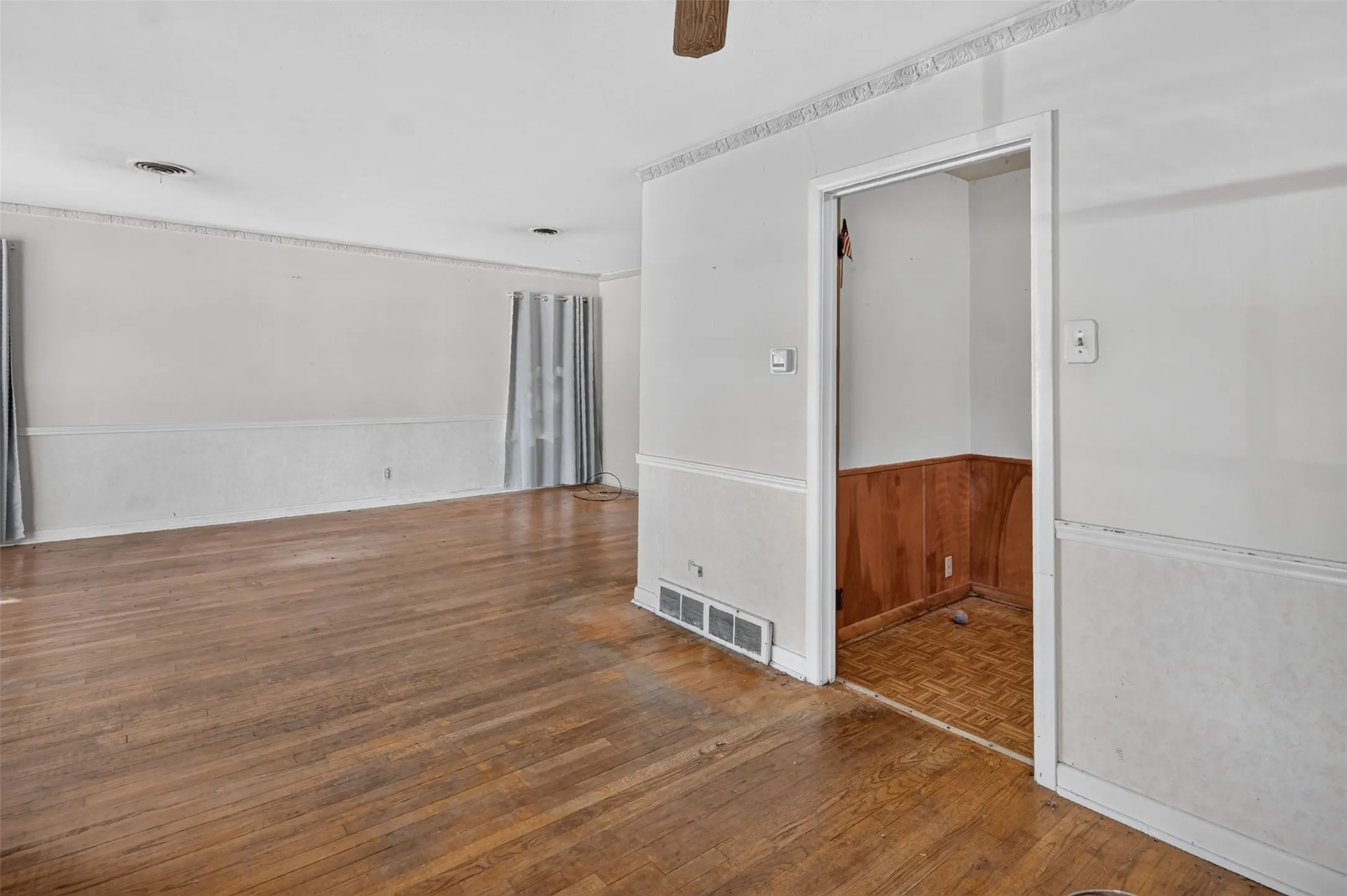 Wood-finish flooring, white walls, decorative crown molding, and white chair rail with textured panels