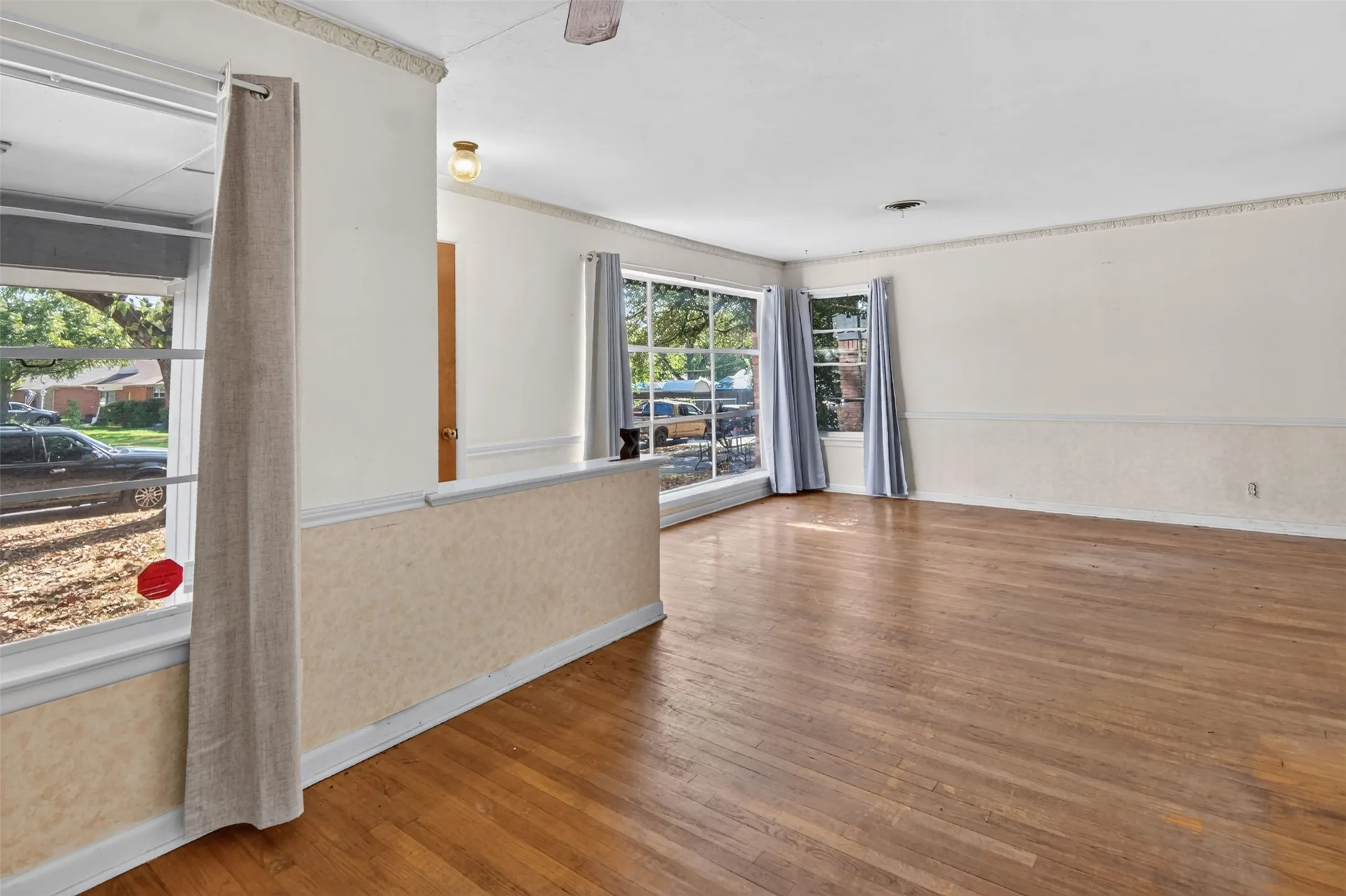 Hardwood flooring throughout, multiple large windows, cased openings, crown molding, and a partial wall with textured detailing