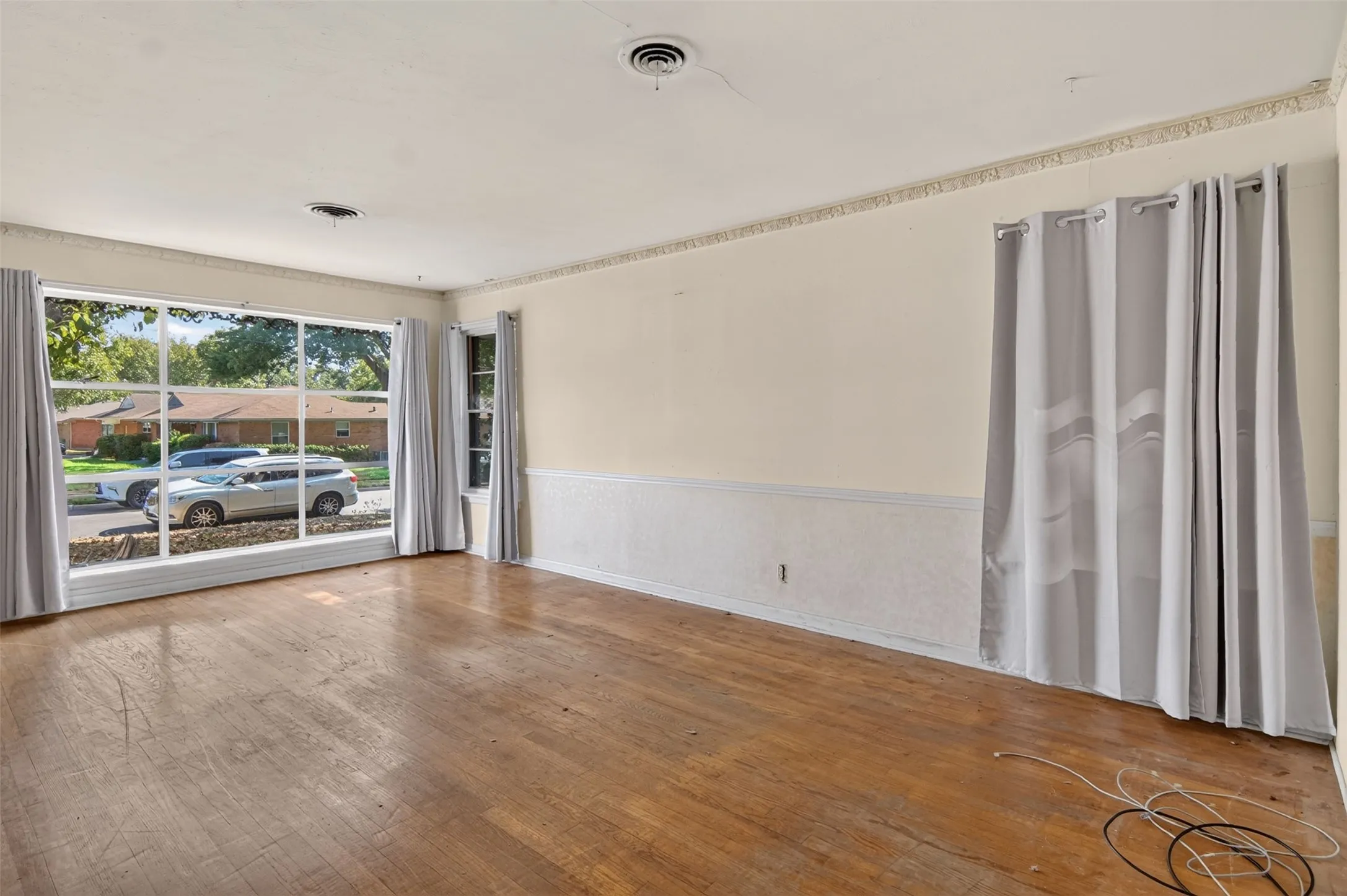 Expansive front window with multiple panes, wood-finish flooring, textured wainscoting, decorative ceiling trim, and multiple wall outlets