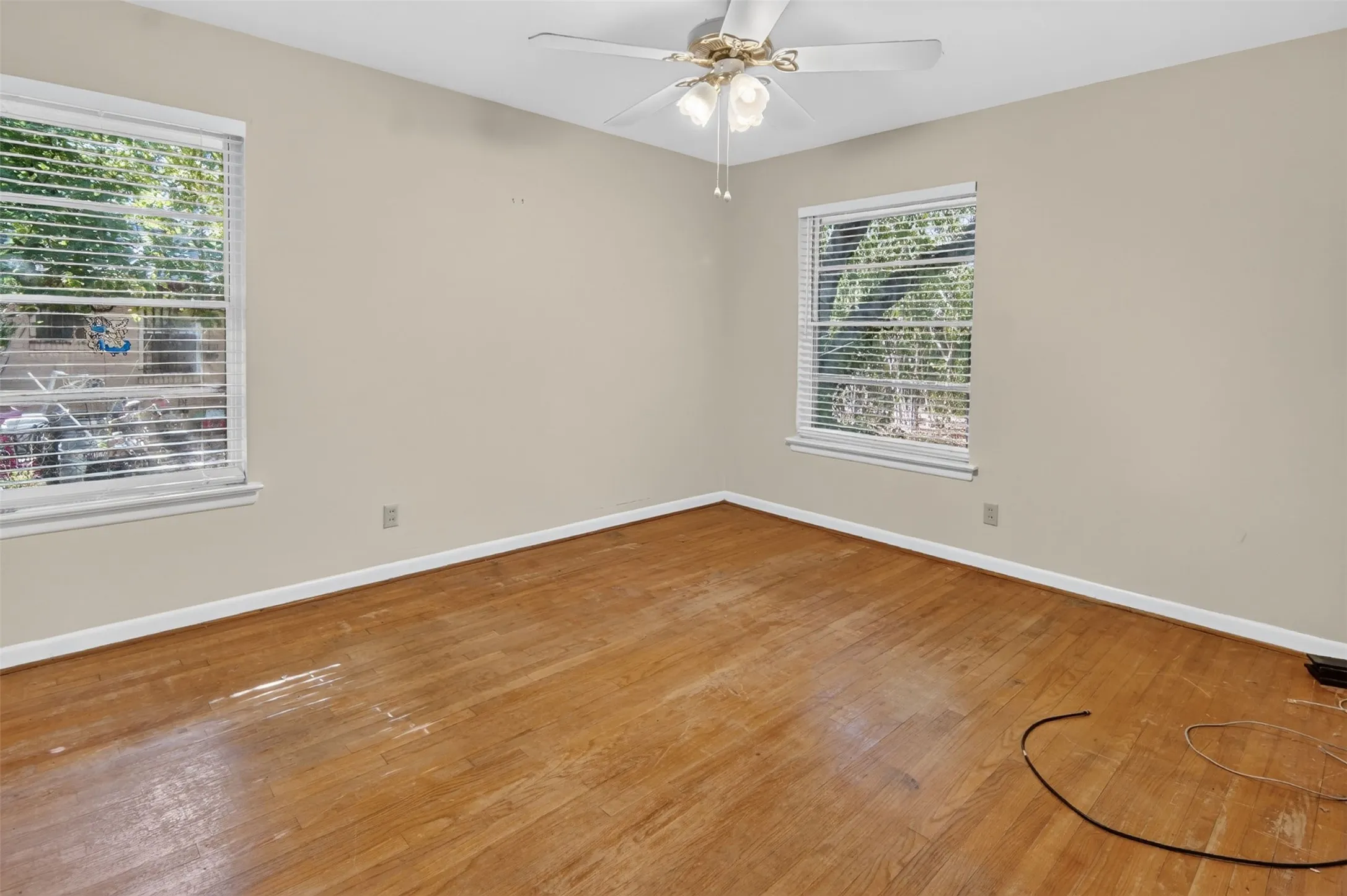 Wood-finish flooring, two windows with blinds, and a ceiling fan with integrated lighting