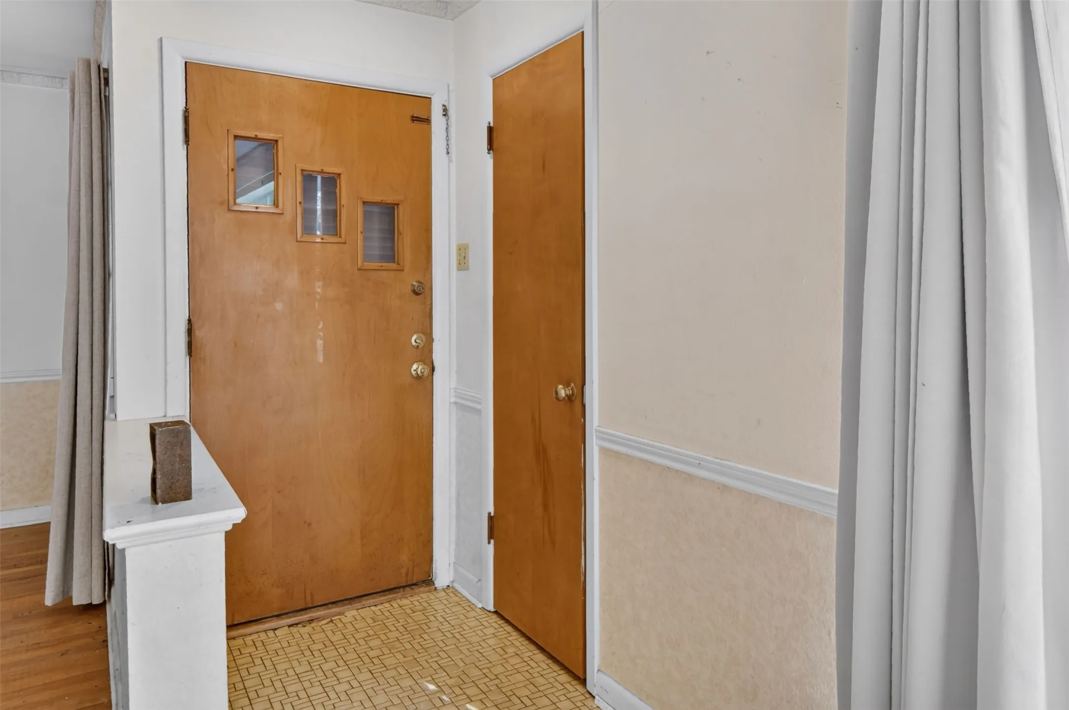 Hardwood entry door with three inset windows, patterned floor tiling, and neutral wall tones