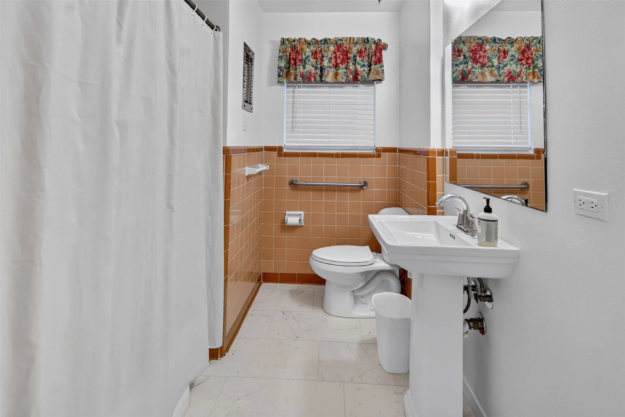 Pedestal sink with chrome faucet, wall-mounted mirror, tiled walls, and window with blinds