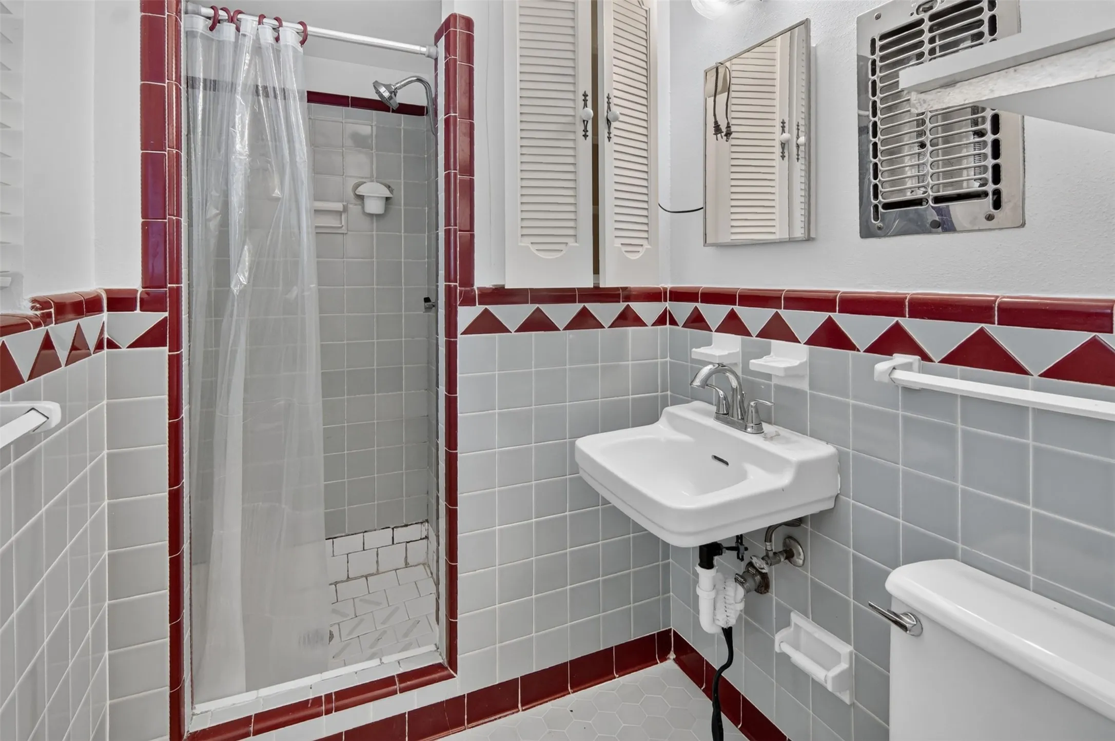 Pedestal sink with chrome fixtures, tiled shower stall, and patterned wall tiling