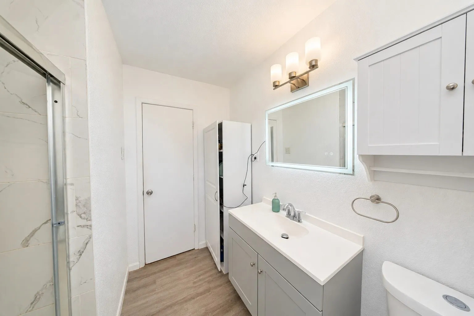 Custom vanity with single basin sink, wall-mounted mirror with integrated lighting, and brushed nickel hardware
