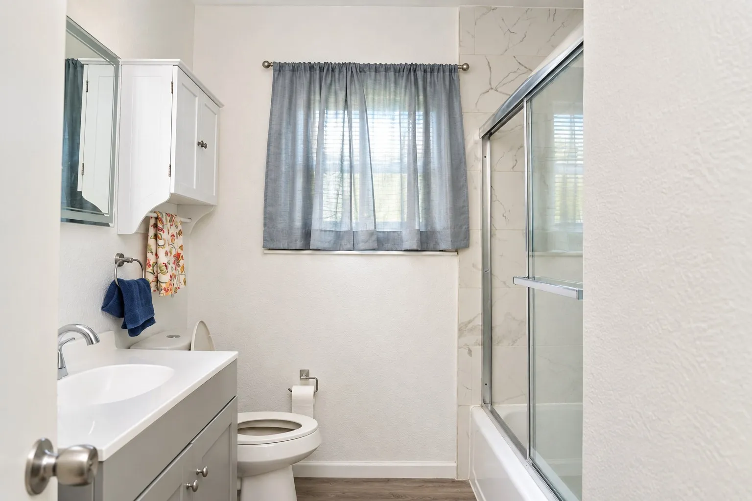 White vanity with integrated sink, chrome faucet, white medicine cabinet, and tub with sliding glass doors