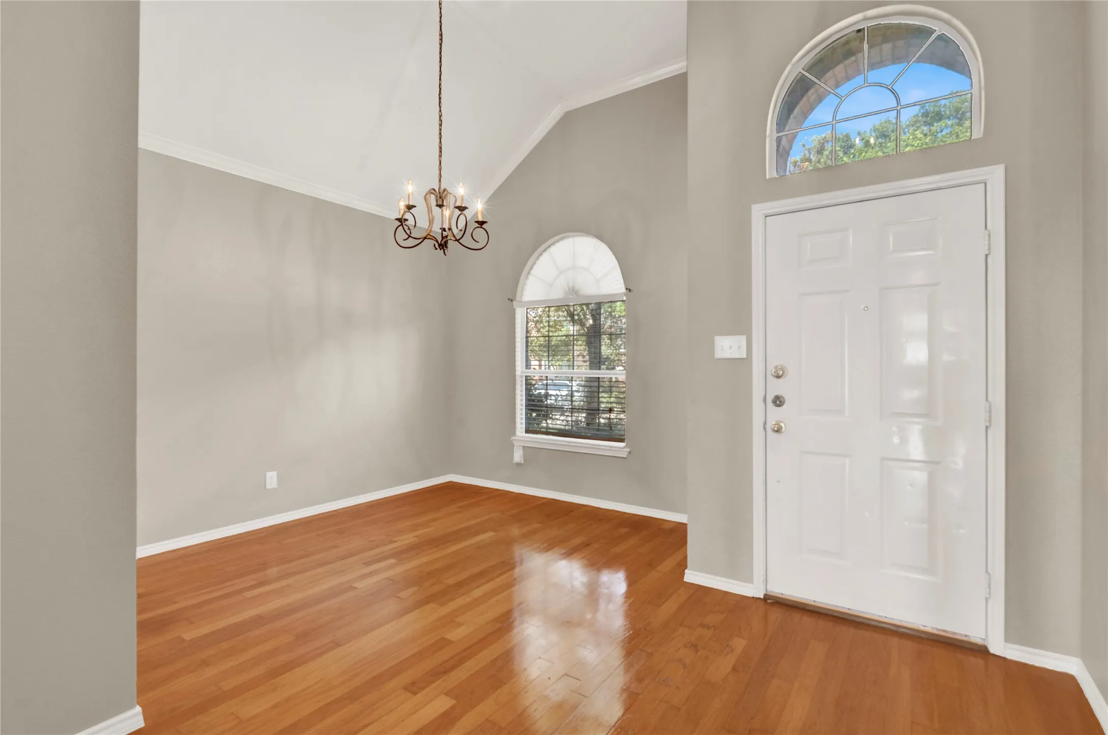 Vaulted ceiling, wood-finish flooring, arched windows, and a decorative chandelier