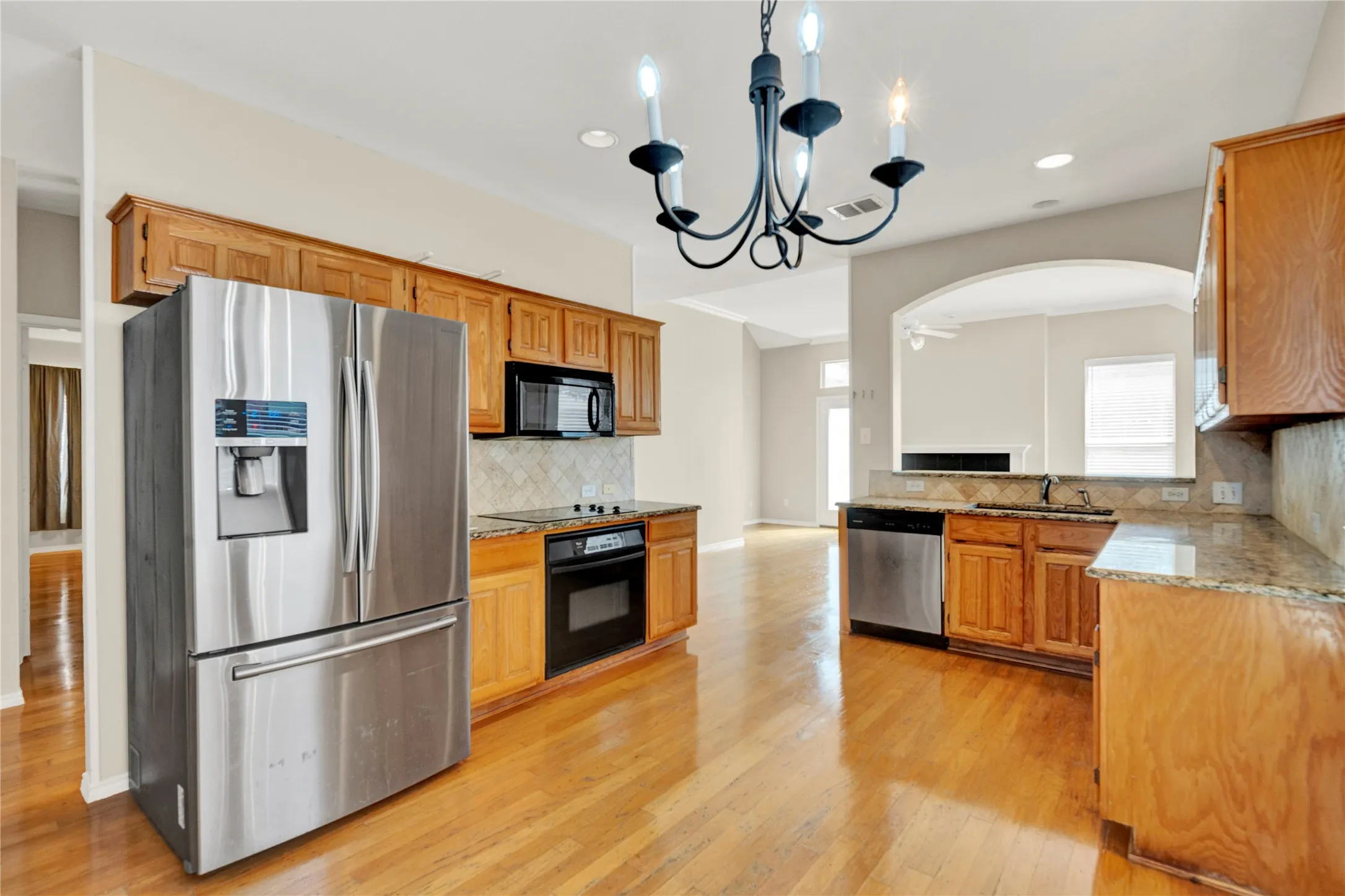 Wood-finish flooring, wood cabinetry, granite countertops, stainless steel appliances, and a decorative chandelier