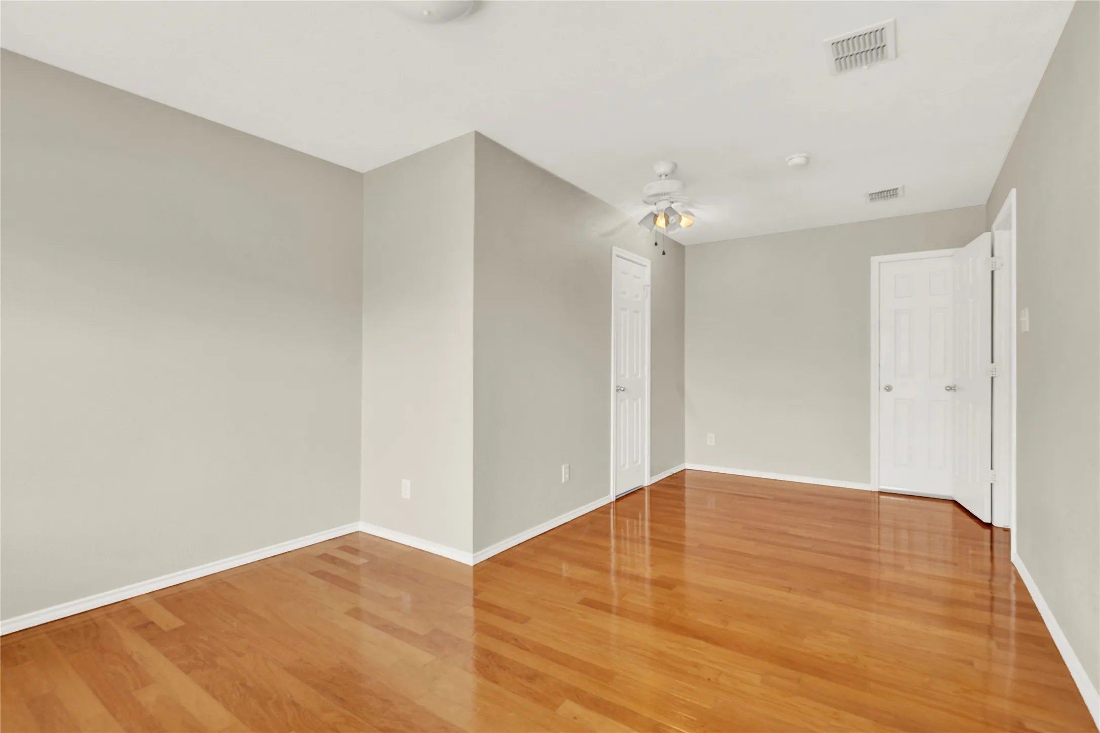 Polished wood-finish flooring, light neutral wall tones, white trim, white paneled doors, and a ceiling fan with integrated lighting