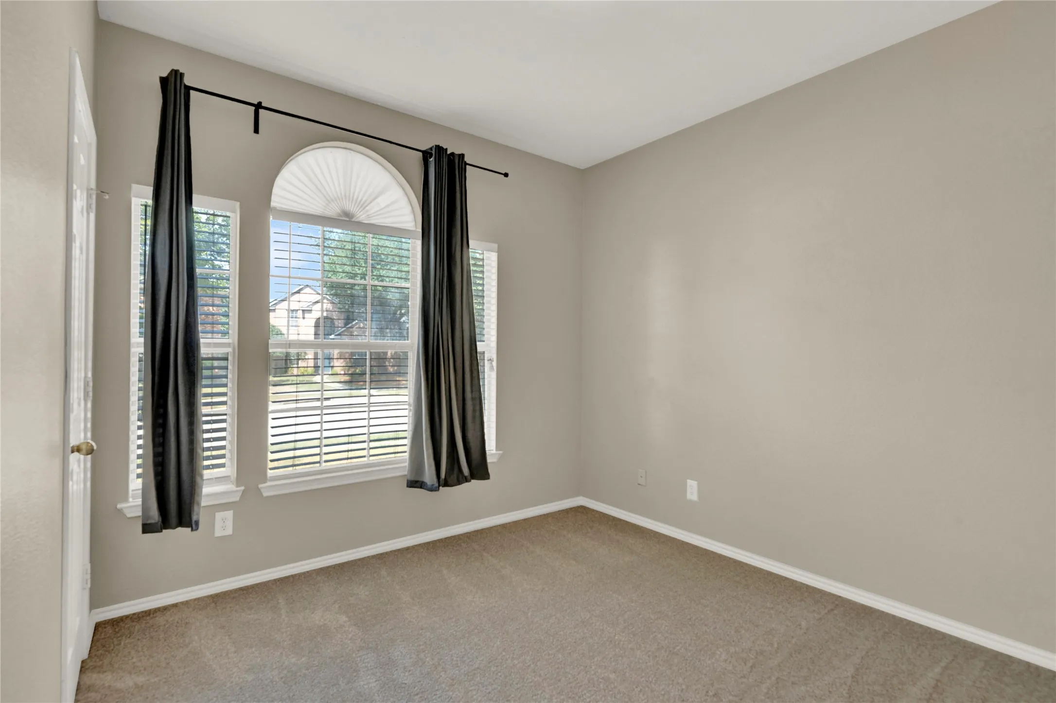 Arched window with two vertical windows, neutral tone carpet, and painted walls