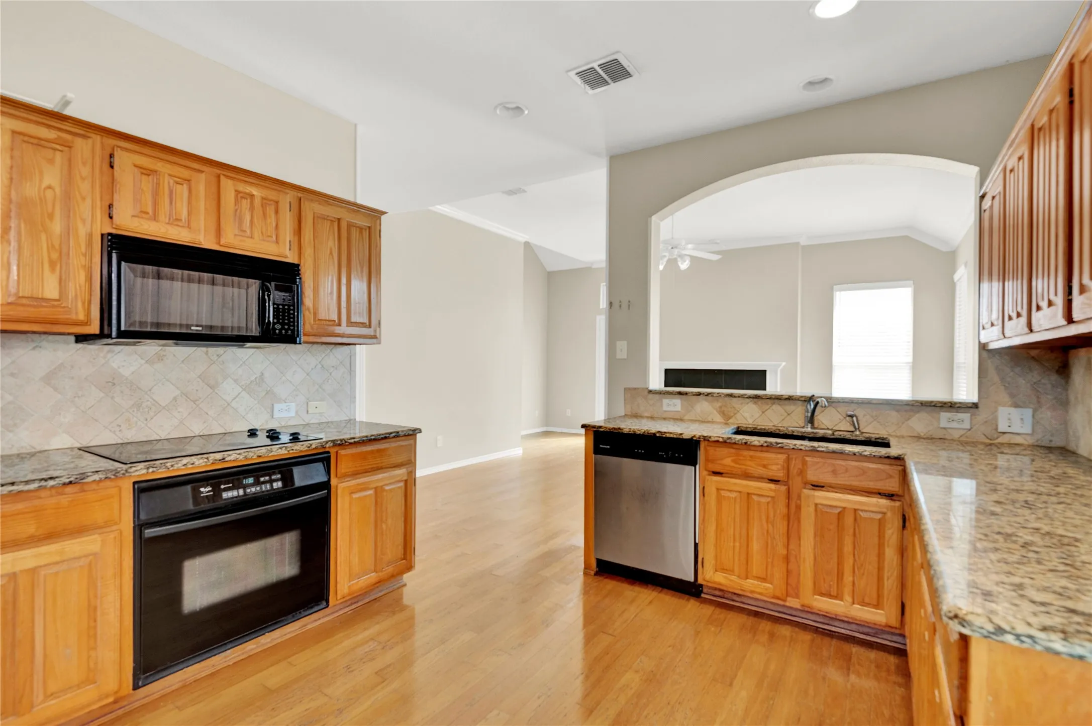 Kitchen featuring wood-finish cabinetry, granite countertops, tile backsplash, stainless steel dishwasher, and built-in microwave