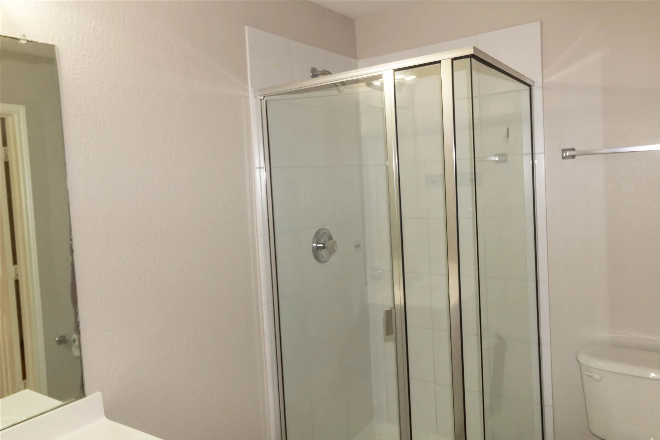 Glass-enclosed shower with a brushed chrome showerhead, white tiled interior, and sliding door