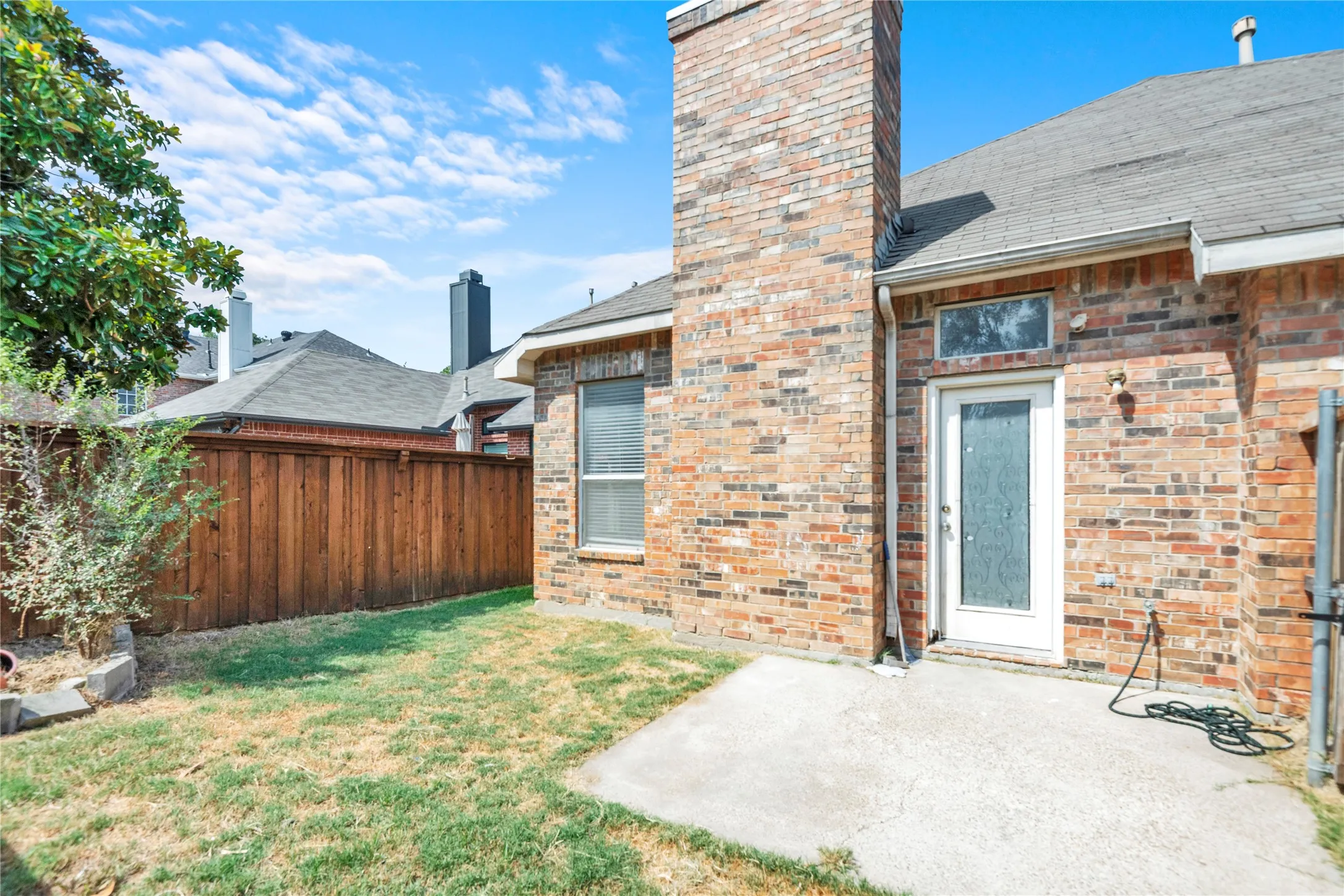 Brick exterior with a prominent chimney, concrete patio area, and a secure wood privacy fence