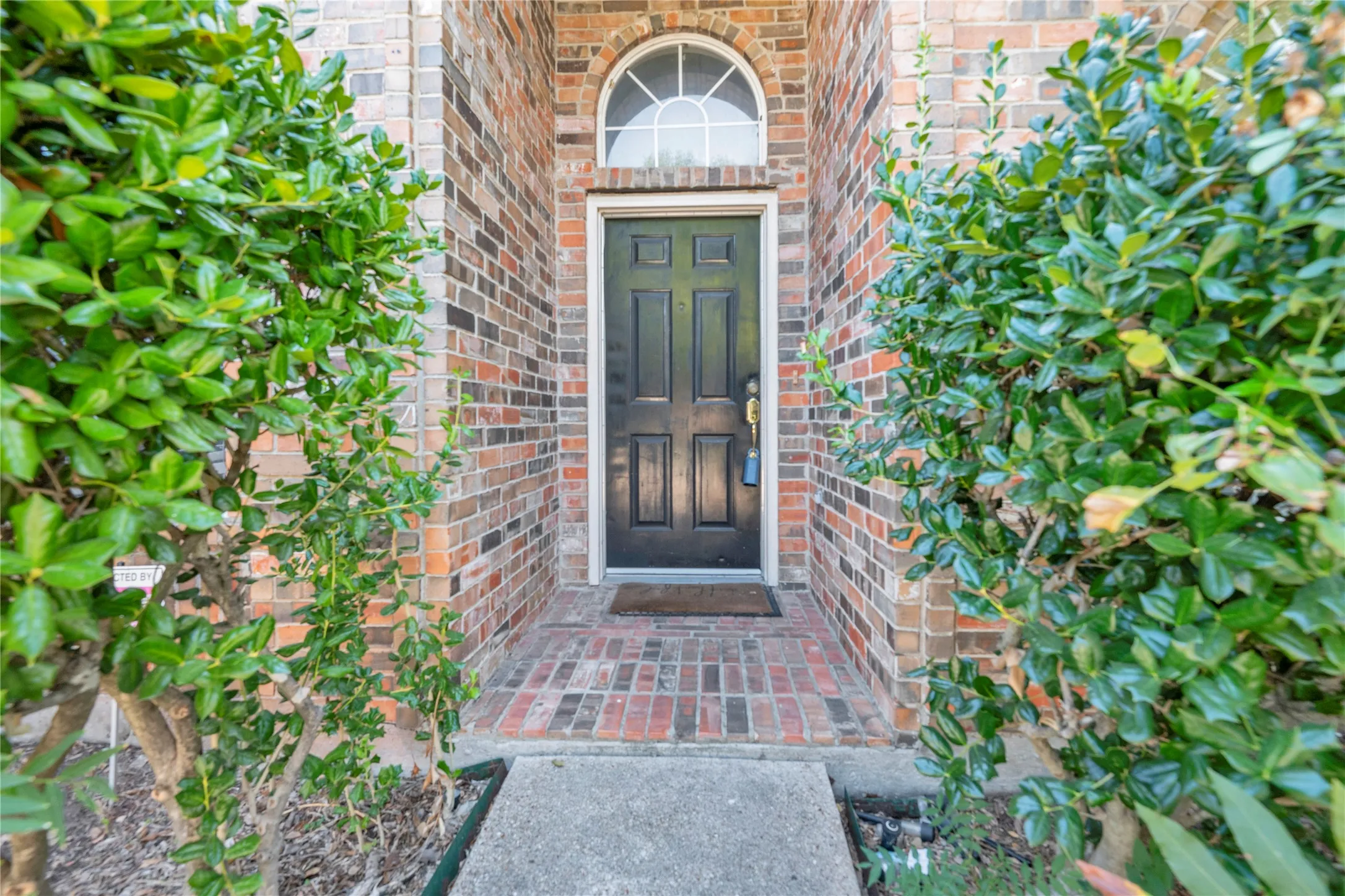 Brick exterior with a dark-paneled door, arched transom window, and a brick paver entryway