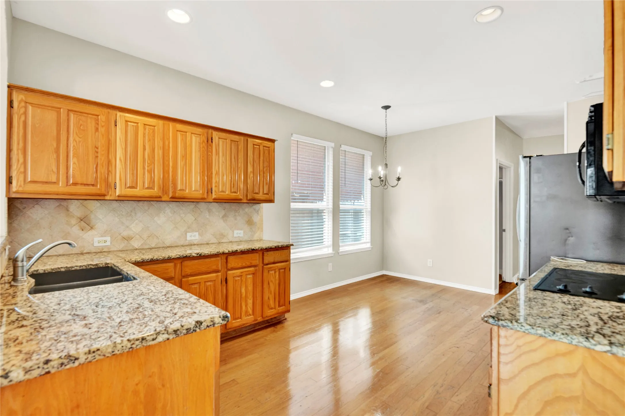 Kitchen with wood-finish flooring, granite countertops, tile backsplash, wood cabinetry, and recessed lighting