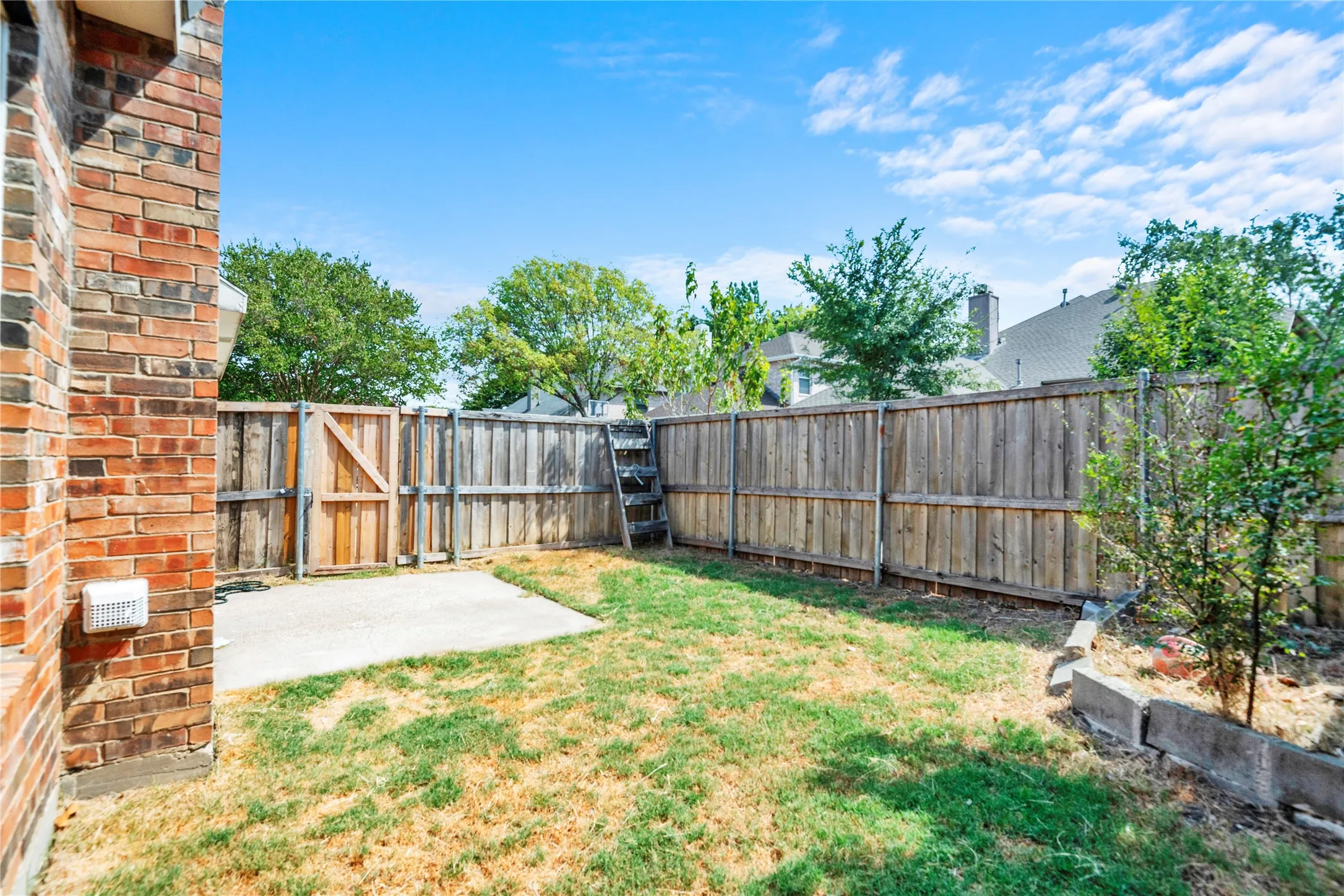 Private backyard with wood fencing, a concrete patio, and brick exterior