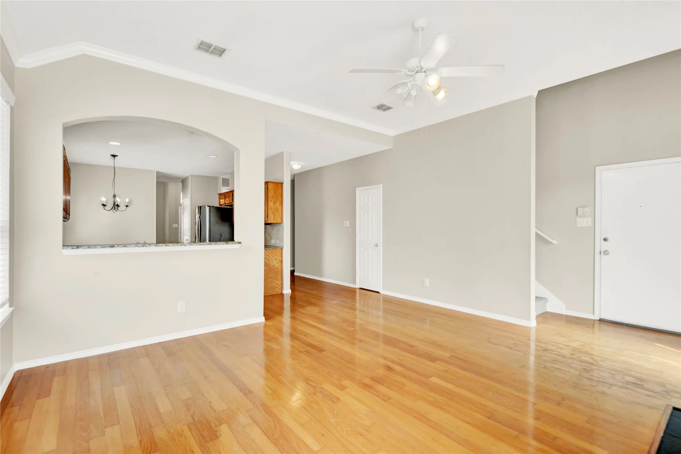 Hardwood flooring, arched pass-through with granite countertop, crown molding, ceiling fan, and staircase