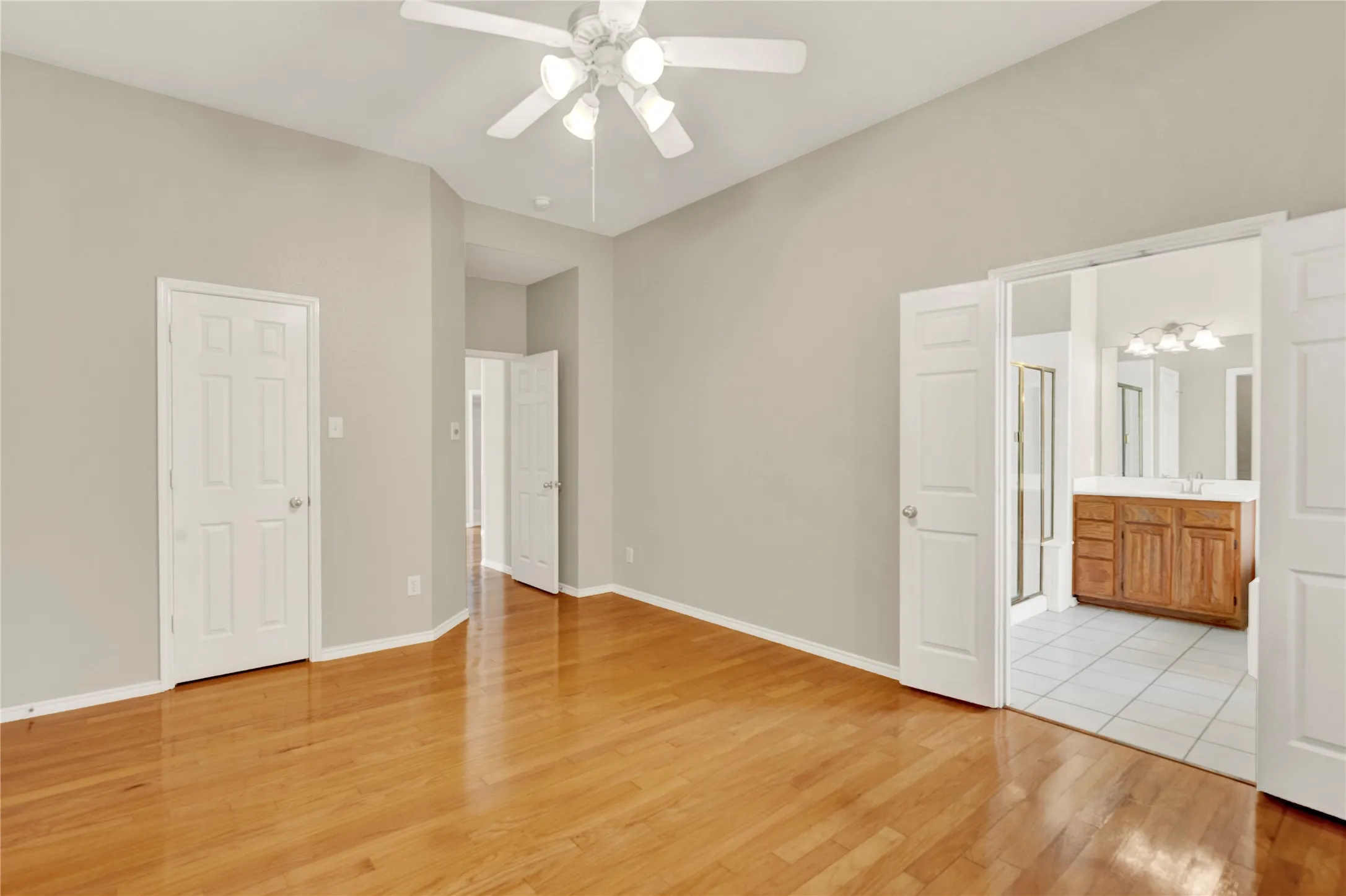 Hardwood flooring, vaulted ceiling, ceiling fan with integrated lighting, wood-finish vanity with dual sinks, and tile flooring