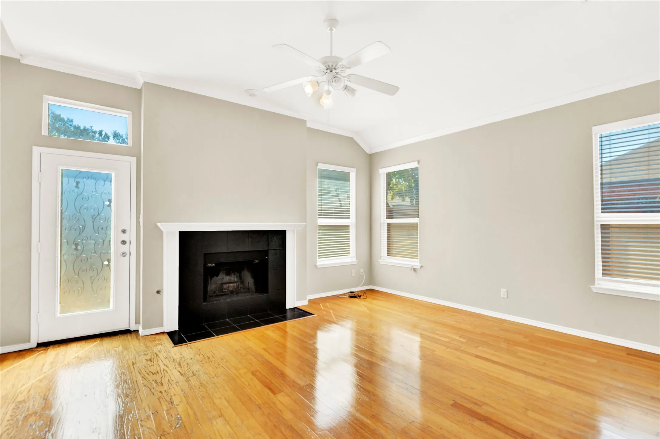 Hardwood flooring throughout, a fireplace with a black tile surround, a white mantel, and multiple windows