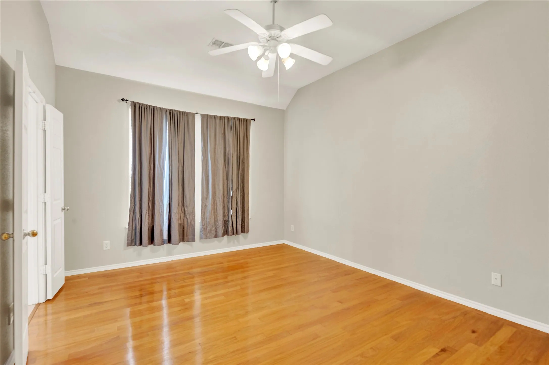 Wood-finish flooring, vaulted ceiling, ceiling fan with integrated lighting, and white bi-fold doors
