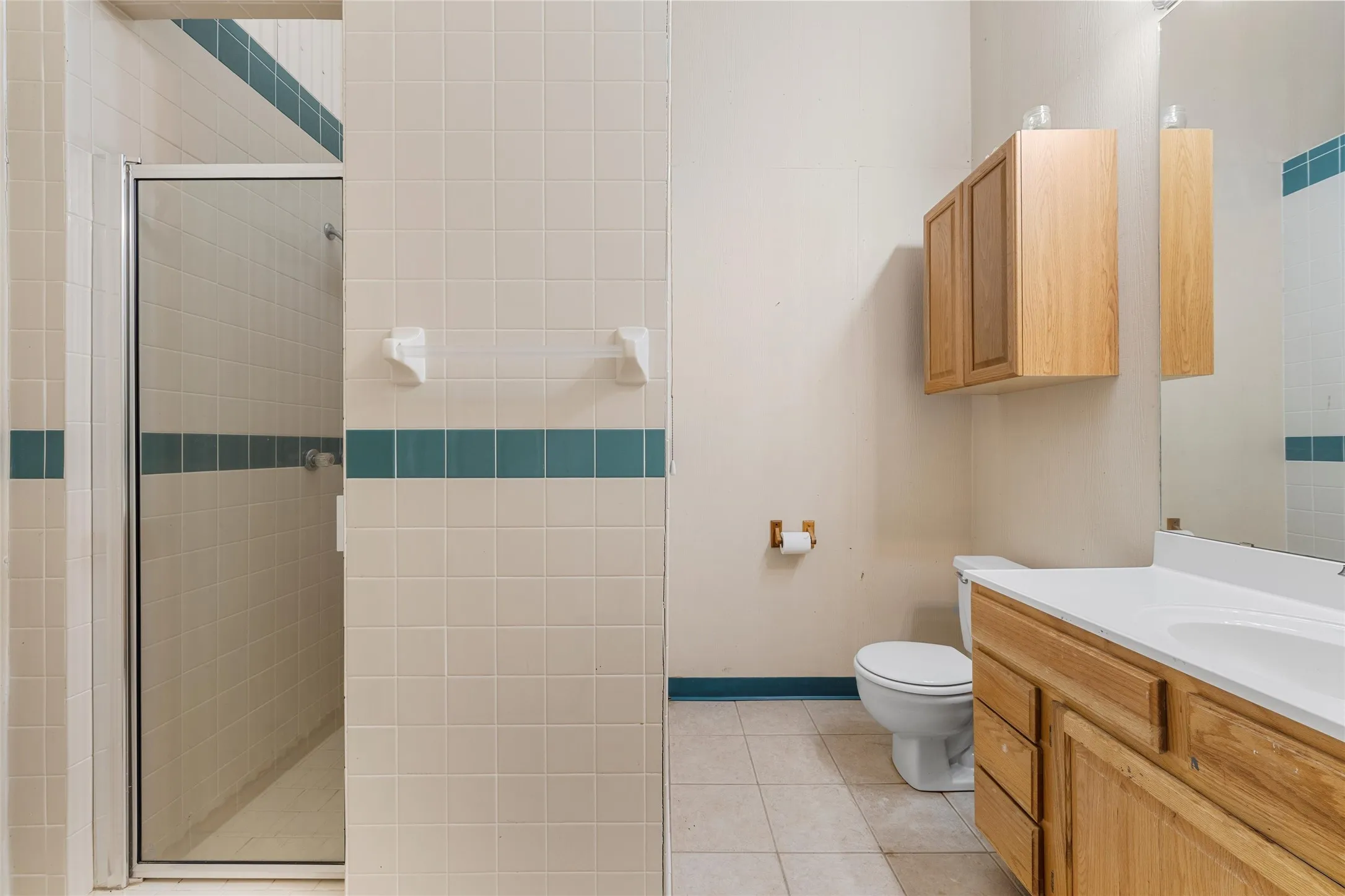 Shower with glass enclosure, single vanity with wood-finish cabinetry, built-in medicine cabinet, and tile flooring