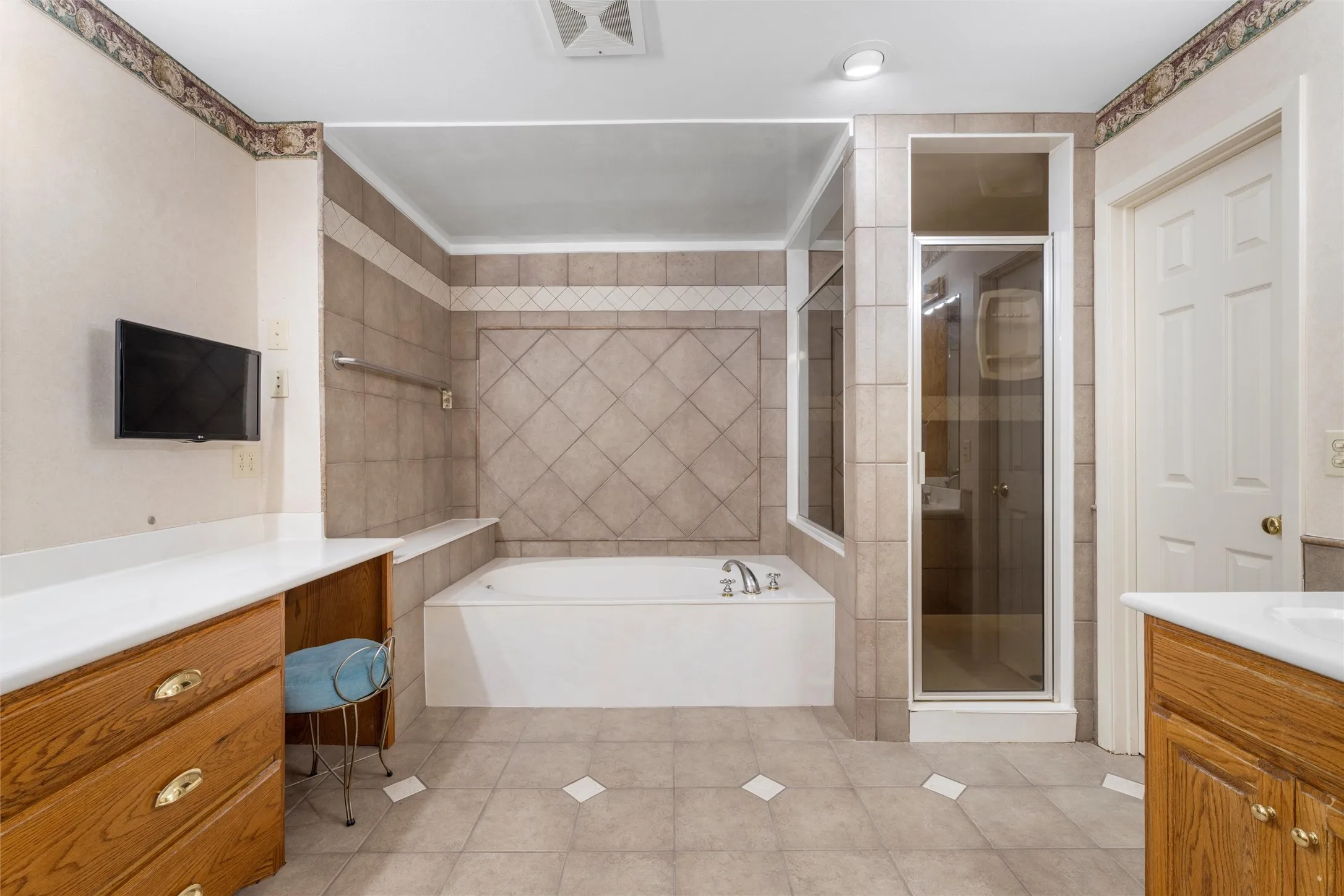 Ceramic tile flooring, tiled shower with glass enclosure, built-in bathtub, wood-finish vanity with countertop, and recessed lighting