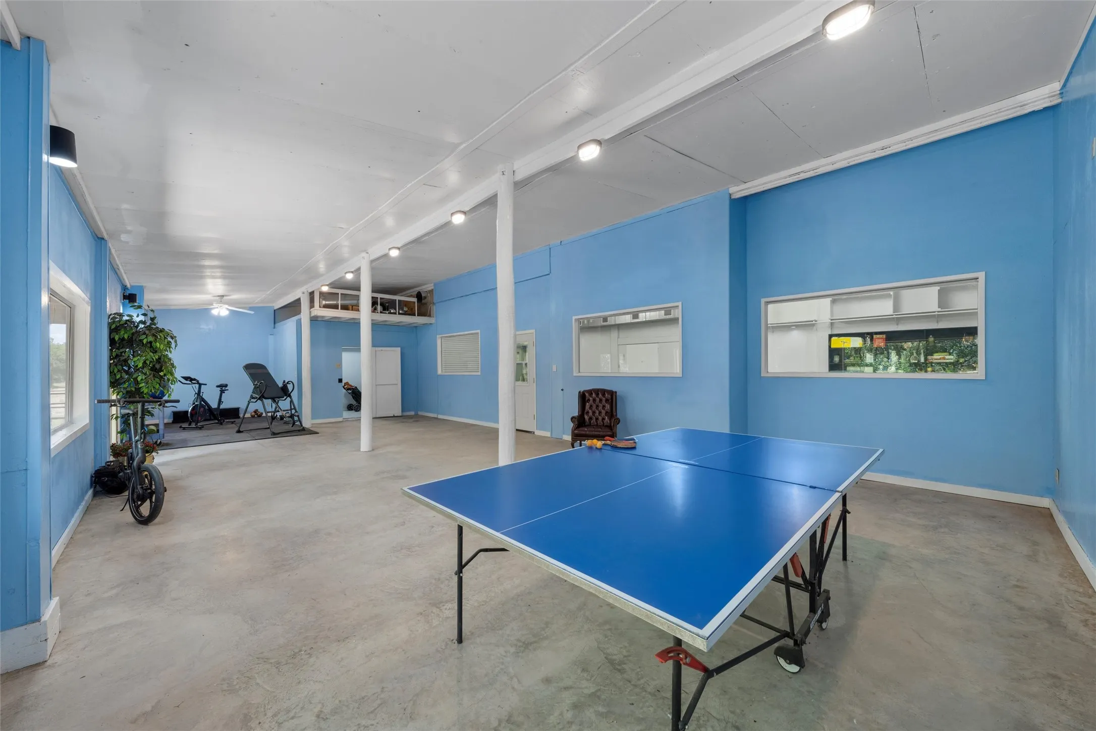 Spacious room featuring light blue walls, concrete flooring, recessed lighting, and support columns