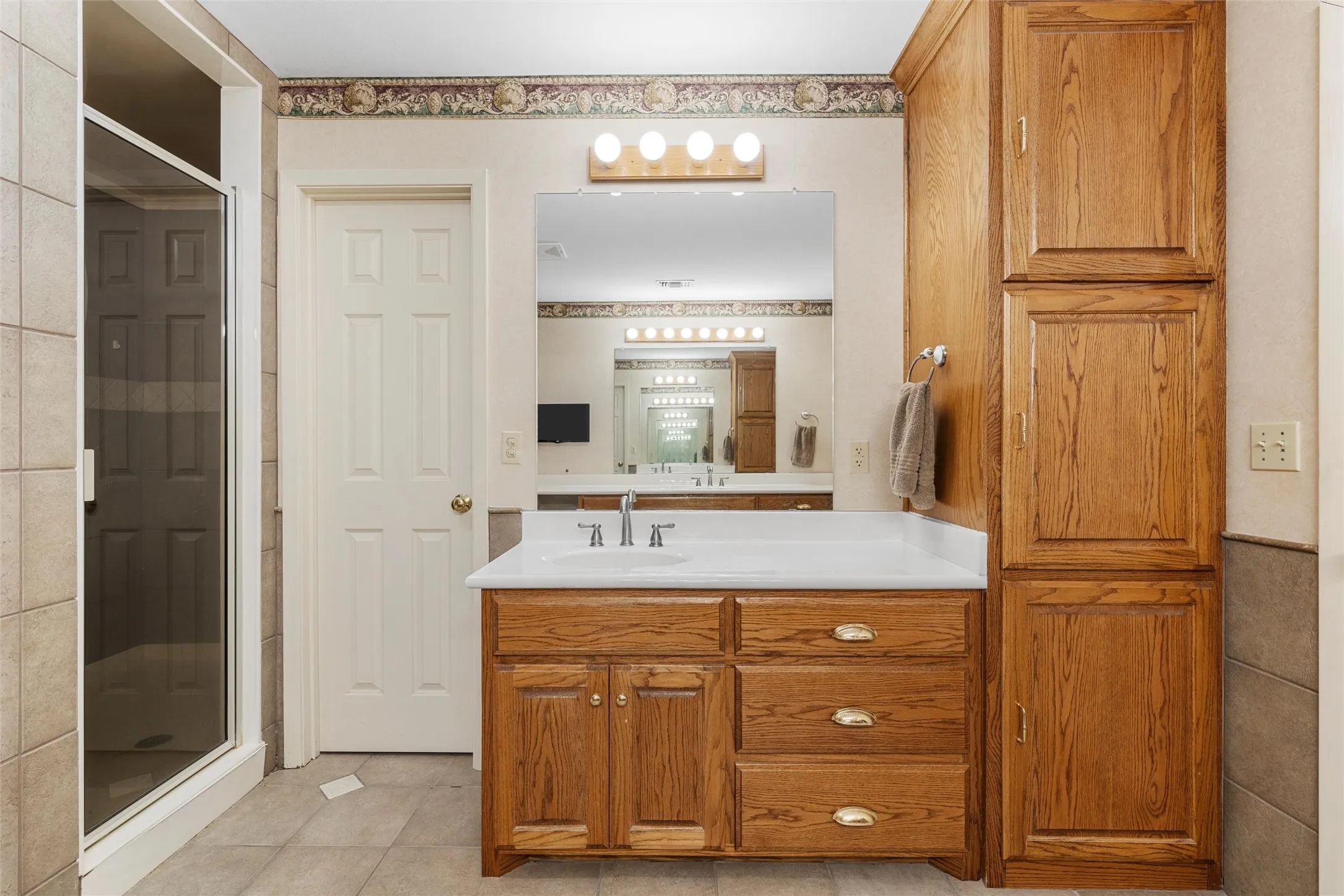 Bathroom featuring a glass-enclosed shower, wood-finish vanity with built-in storage, white countertop, and large wall-mounted mirror