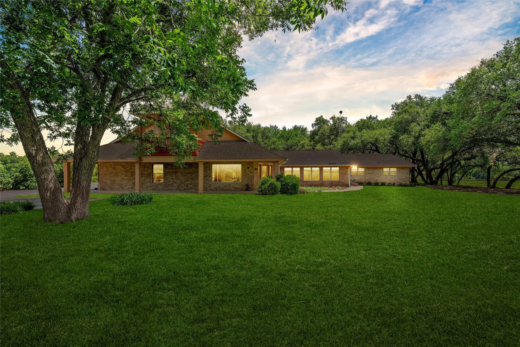 Expansive front lawn with mature trees, brick exterior, covered front porch, and multiple windows