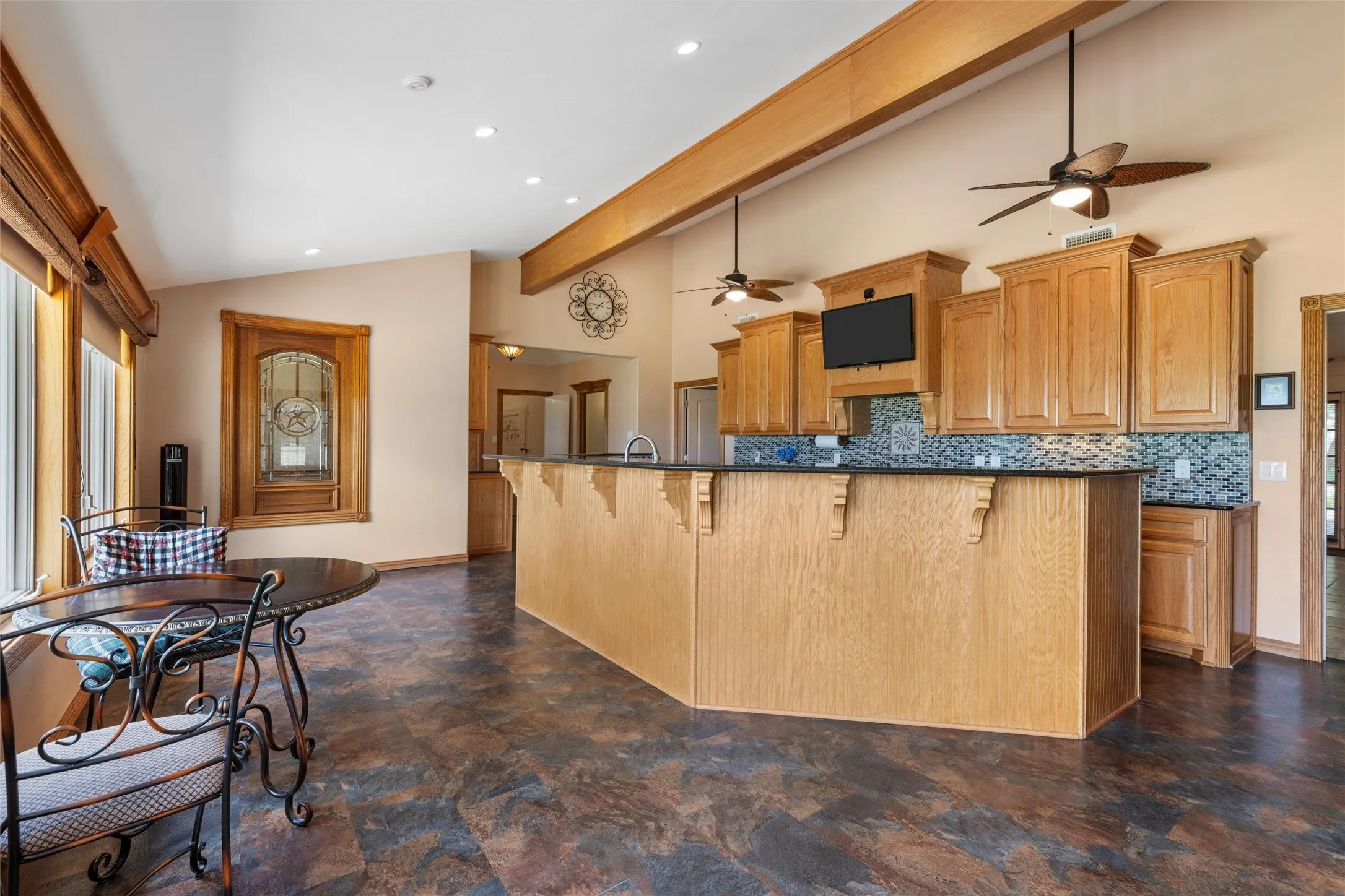 Vaulted ceilings, exposed wood beams, wood-finish cabinetry, patterned backsplash, and a breakfast bar