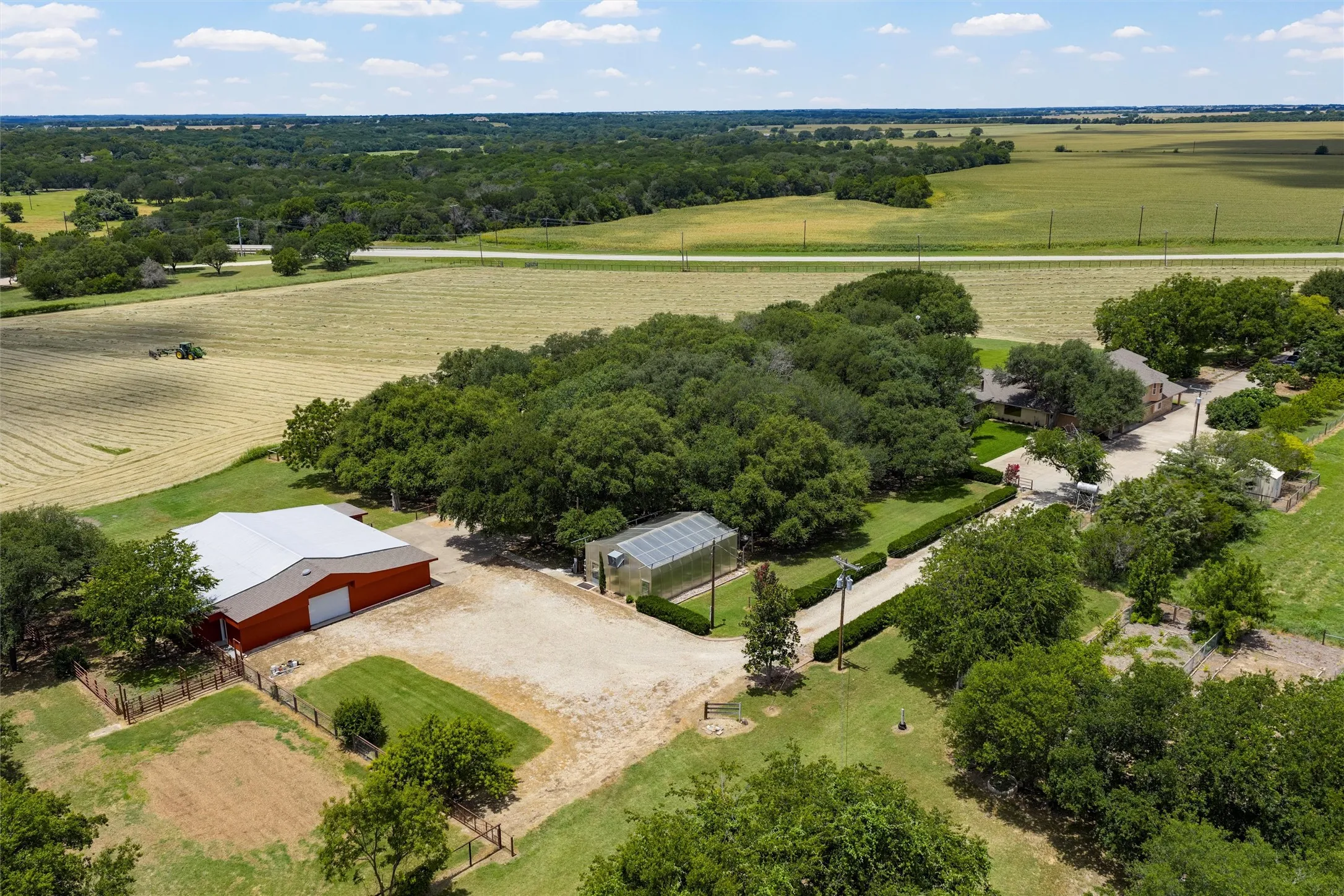 Expansive property featuring a red barn with a metal roof, a greenhouse, a gravel driveway, and mature landscaping