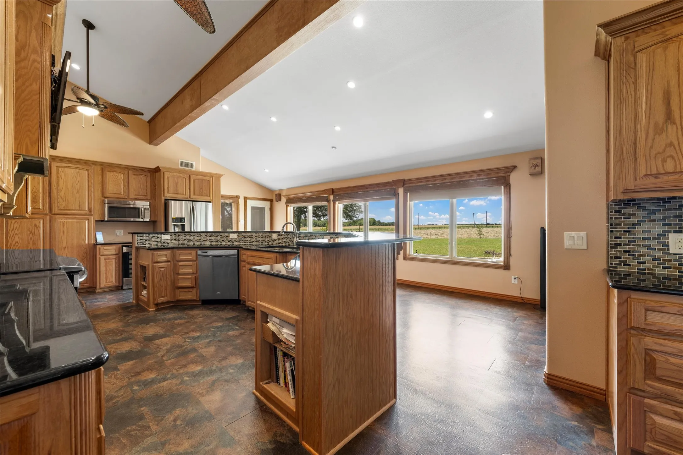 Spacious kitchen featuring wood cabinetry, dark countertops, built-in stainless steel appliances, and a vaulted ceiling with exposed beams