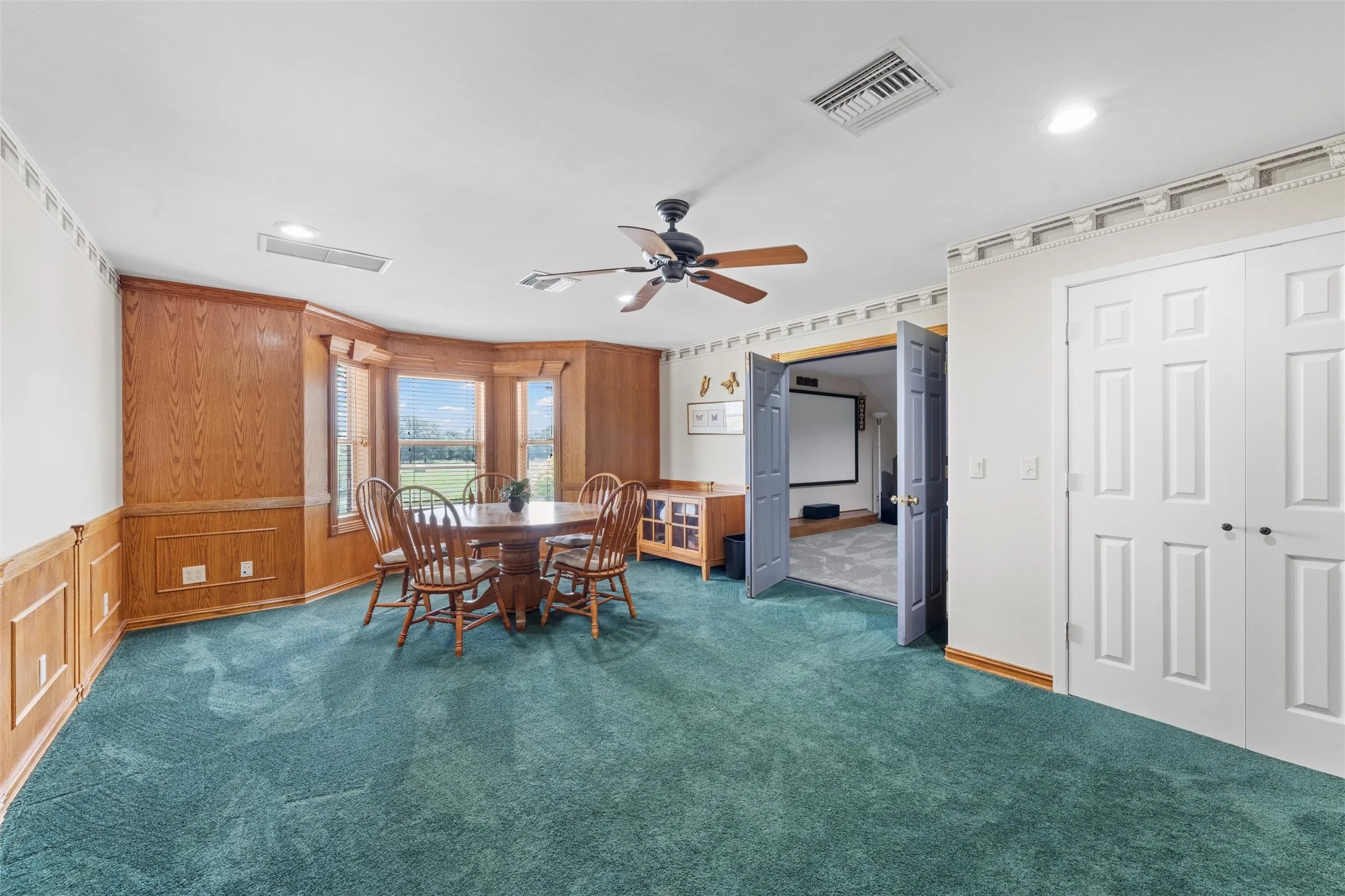Bay window with exterior views, wood paneling, ceiling fan, carpet flooring, and double bi-fold doors