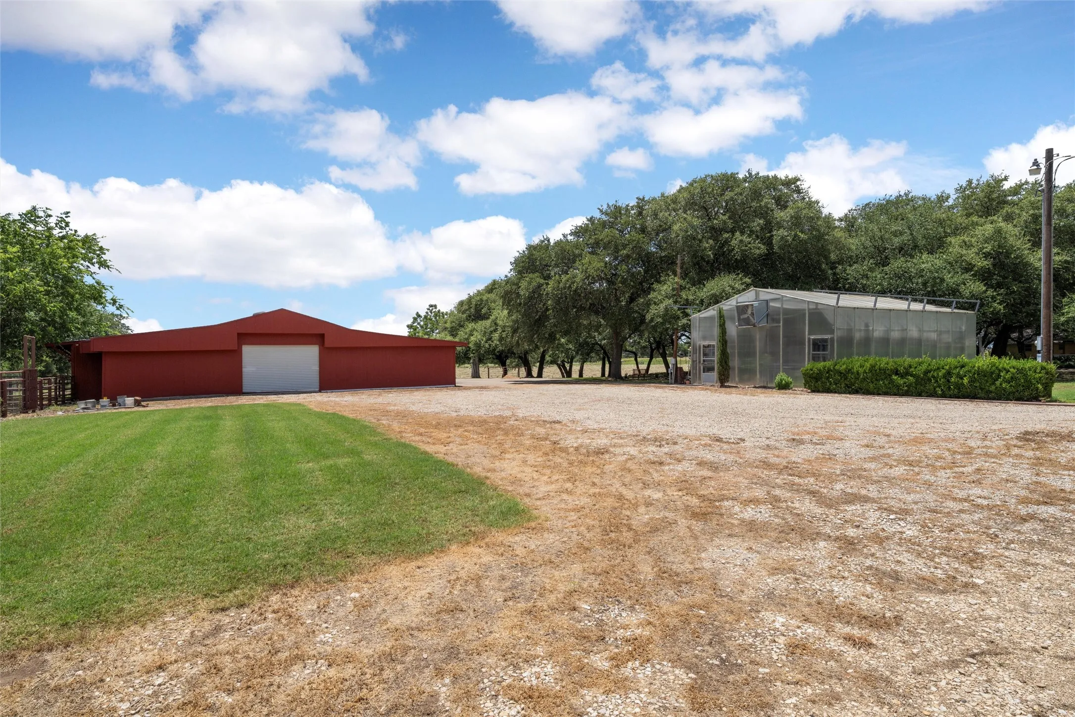 Red barn structure, gravel yard, glass greenhouse, manicured shrubbery, mature trees