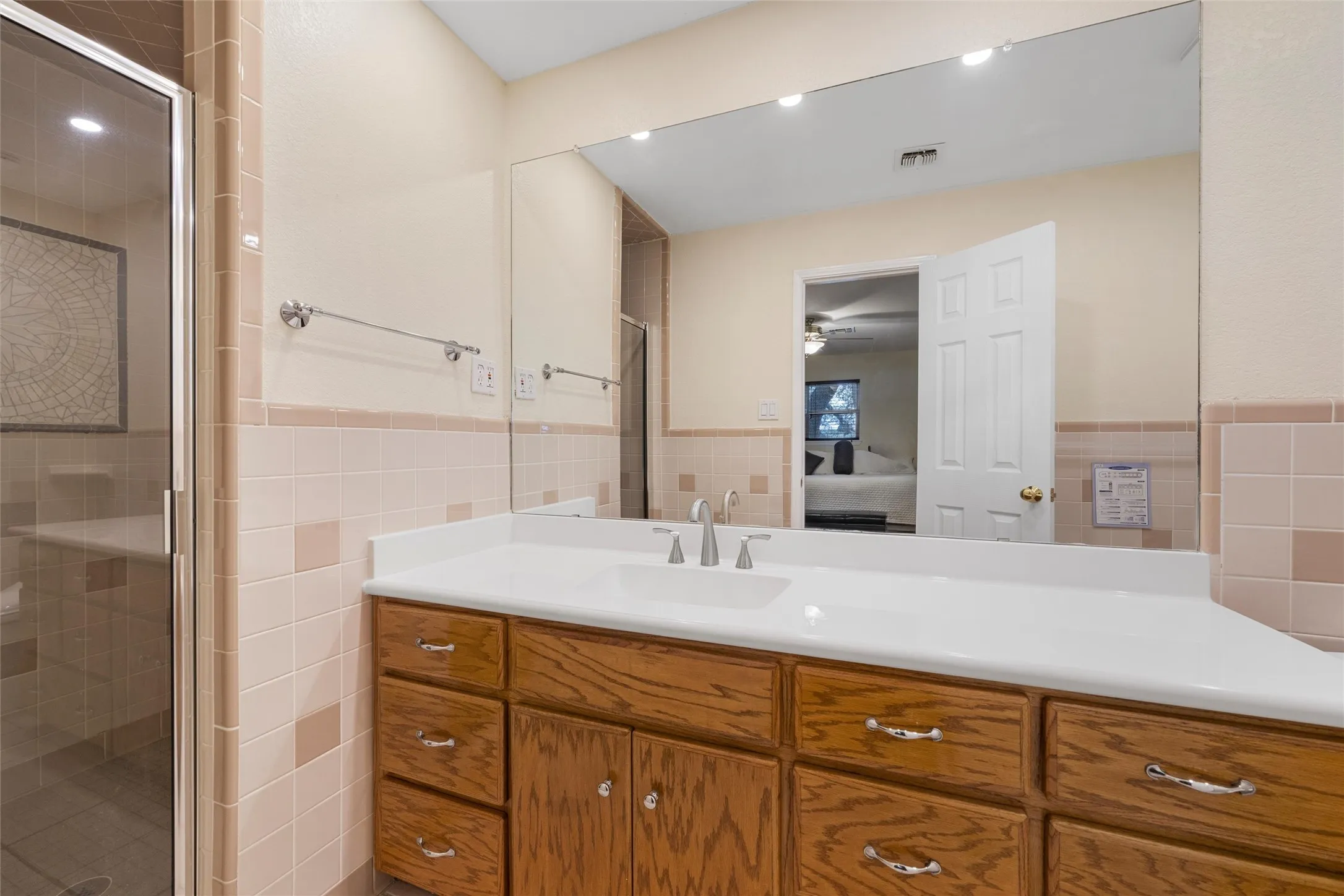 Wood-finish vanity with ample storage, large vanity mirror, recessed lighting, and a glass-enclosed shower