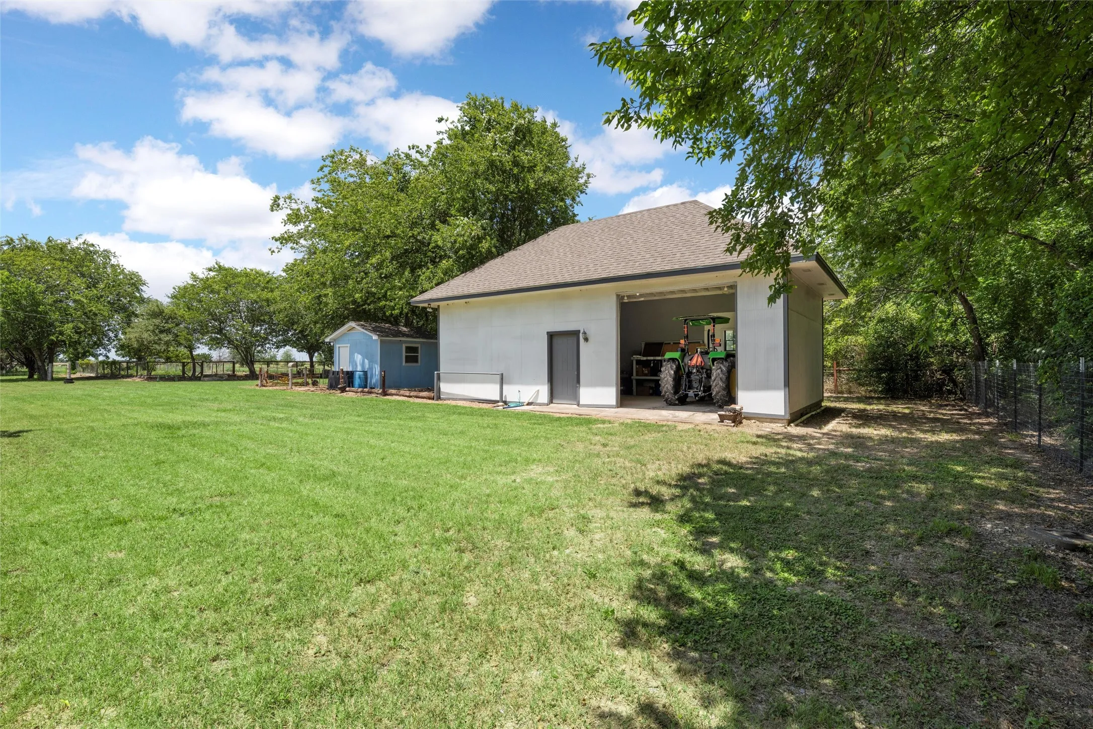 Expansive grass lawn with a detached storage building, a separate utility shed, and mature trees