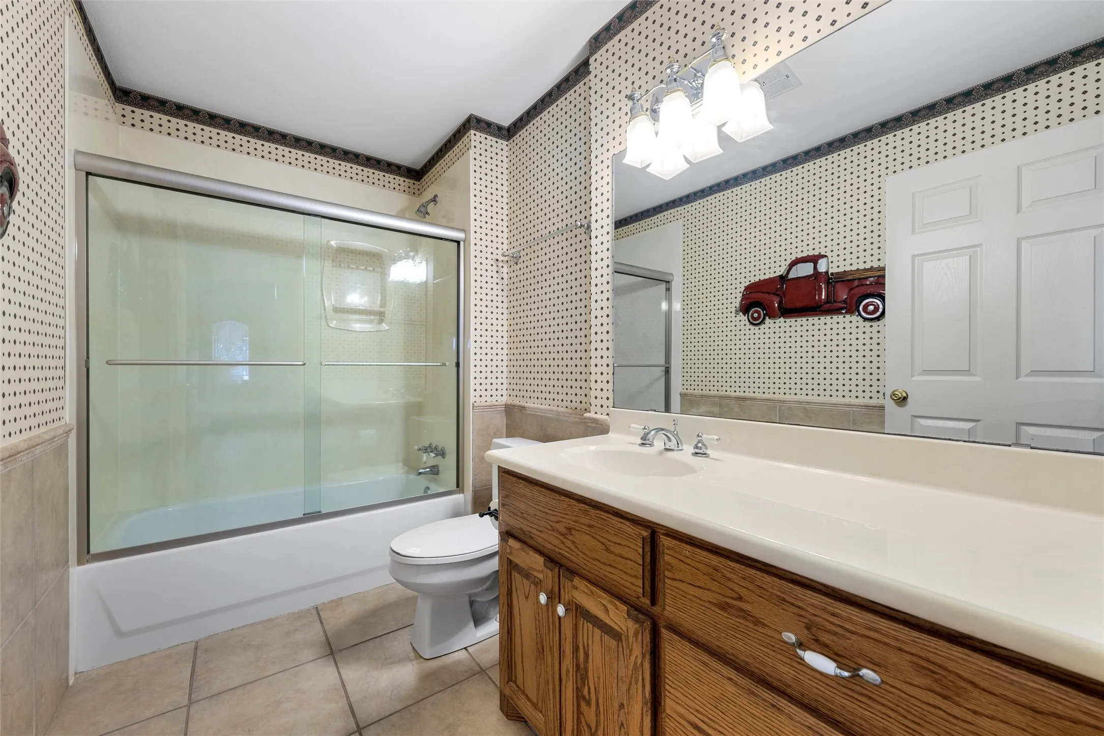 Tub and shower combination with sliding glass doors, single vanity with integrated sink, wood-finish cabinetry, and tiled flooring