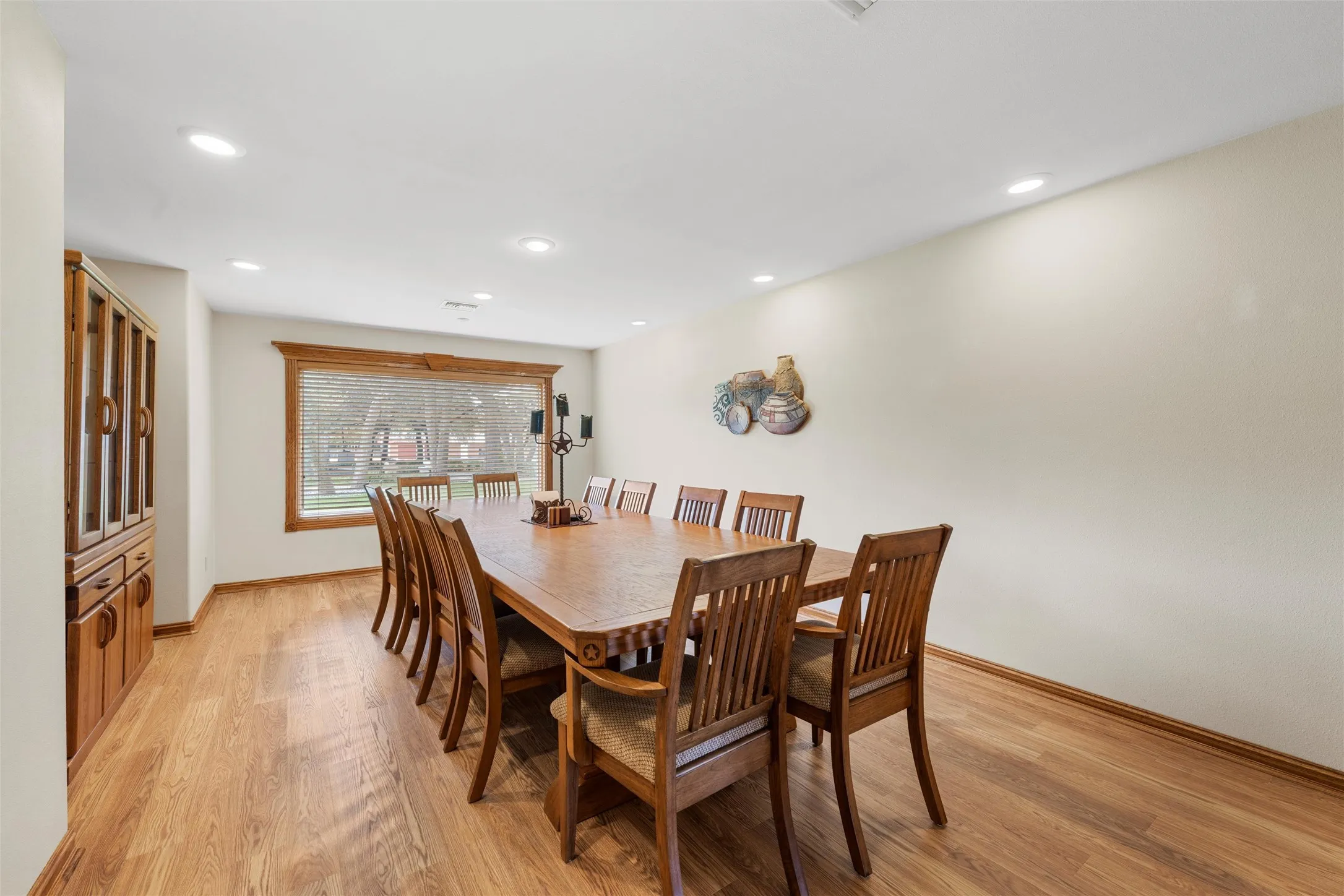 Spacious dining area featuring wood-finish flooring, recessed lighting, a large window with wood trim, and a built-in display cabinet