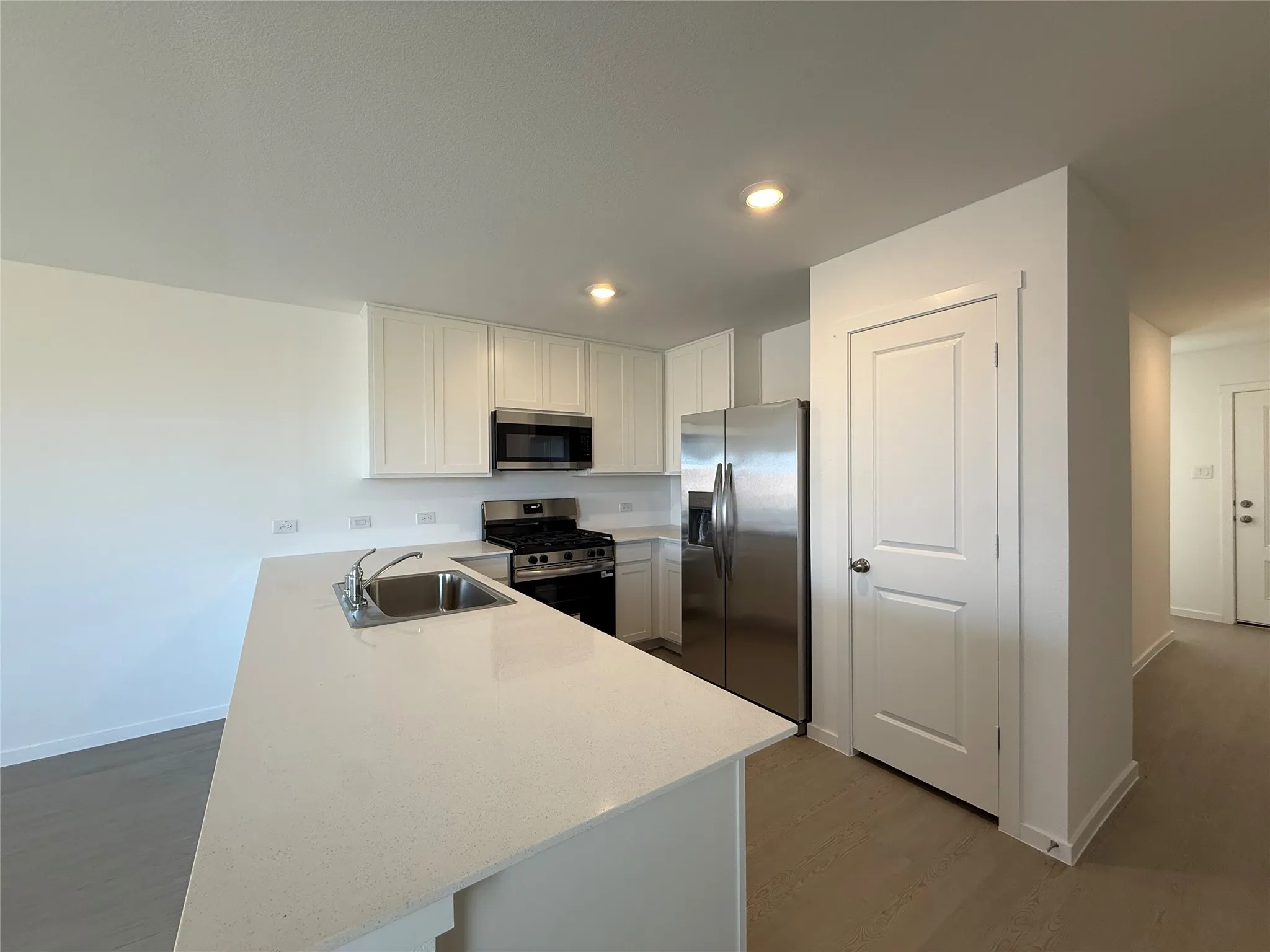 Kitchen featuring white cabinetry, stainless steel appliances, a kitchen island with an undermount sink, and light wood-finish flooring