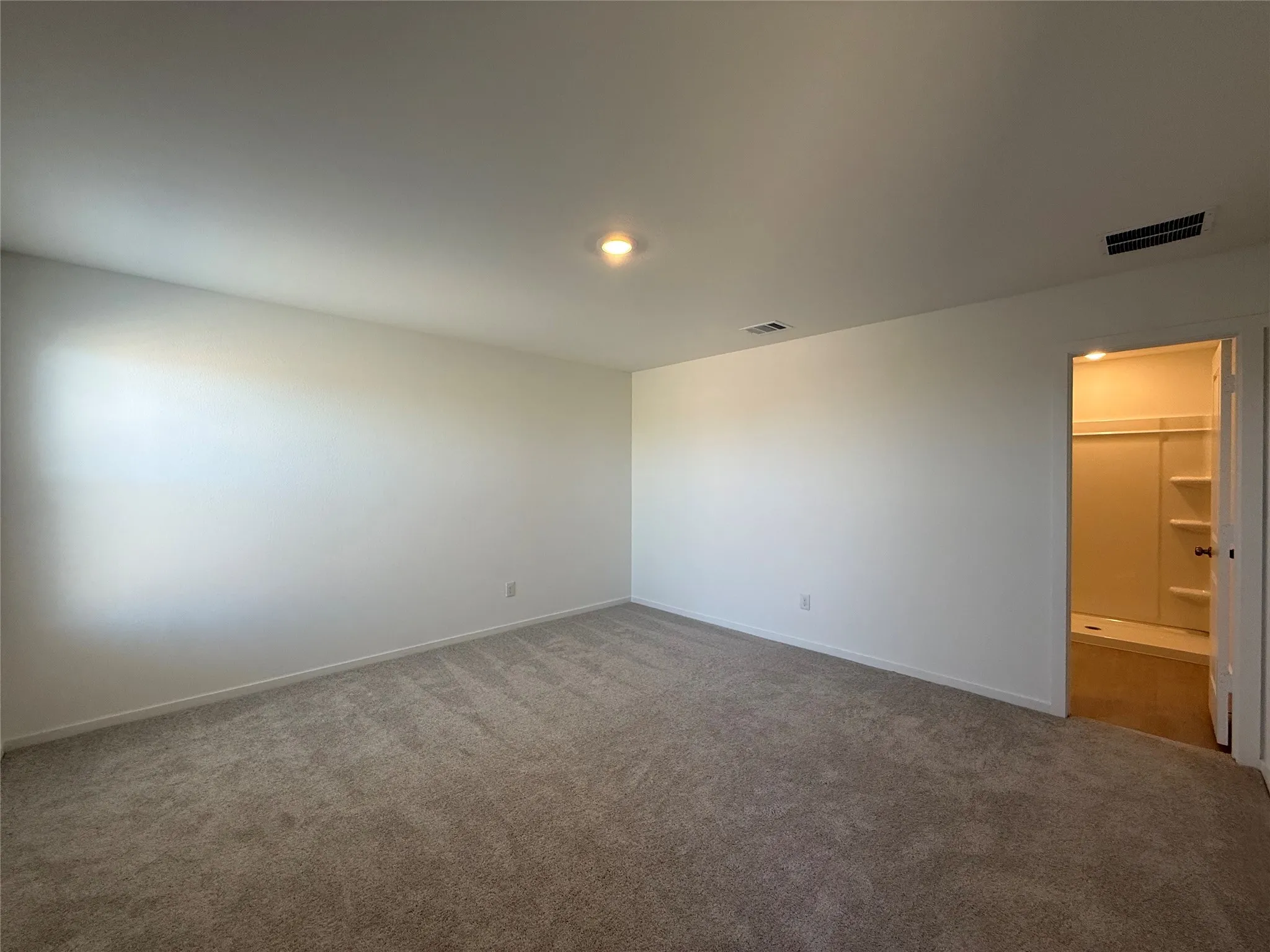 Spacious carpeted room featuring a ceiling-mounted light fixture and doorway access to a full bathroom