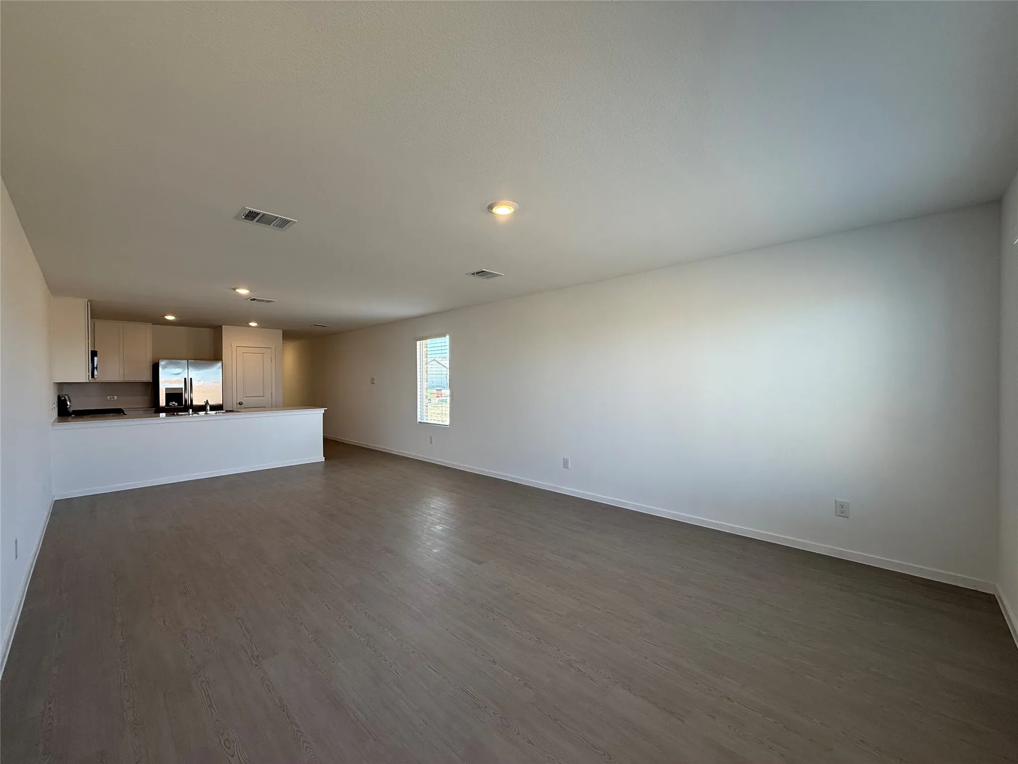 Open-concept living space featuring wood-finish flooring, recessed lighting, and a kitchen with stainless steel appliances, light cabinetry, and a peninsula