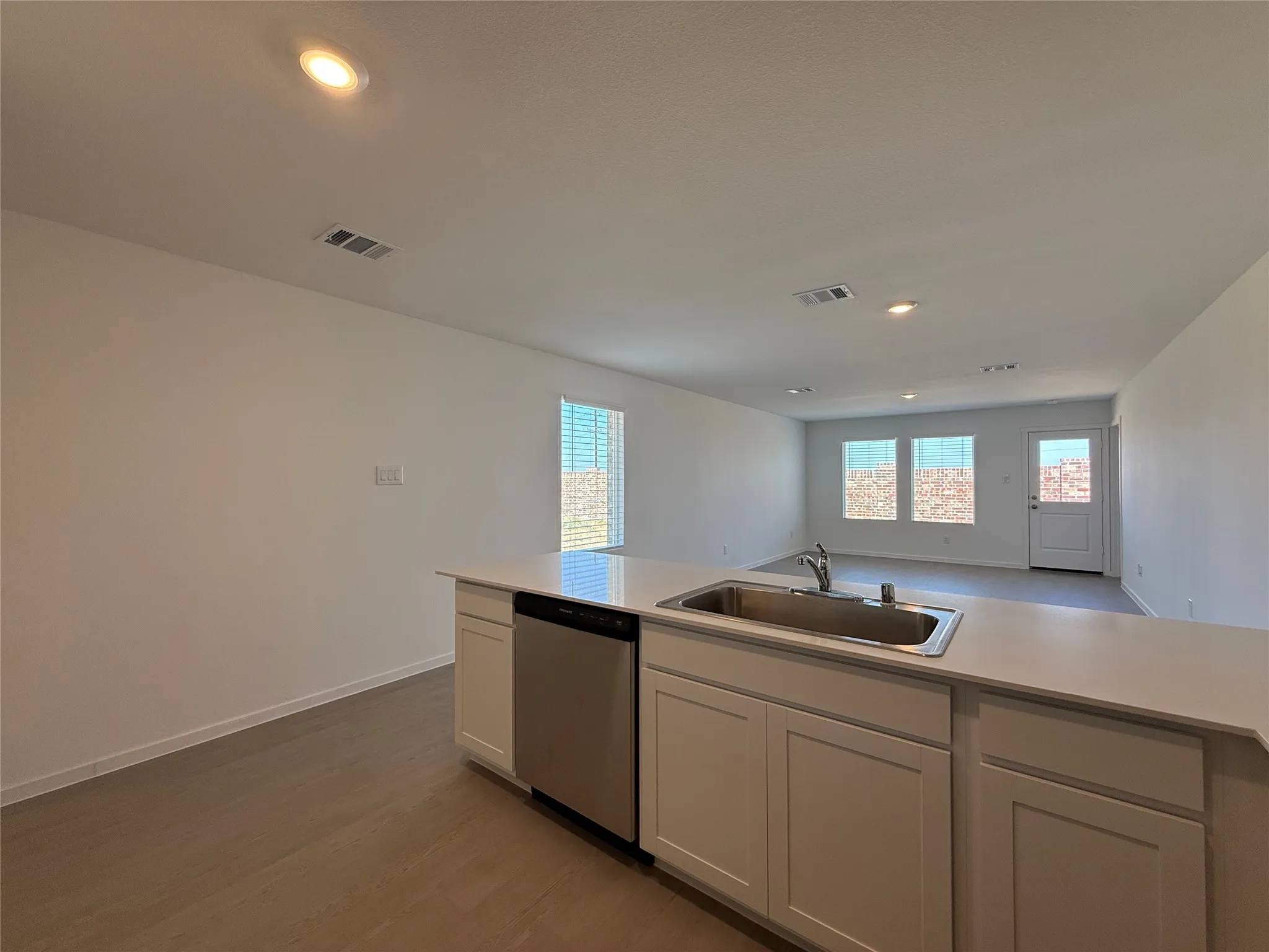 Kitchen island with an undermount sink, stainless steel dishwasher, white cabinetry, and light-colored countertops