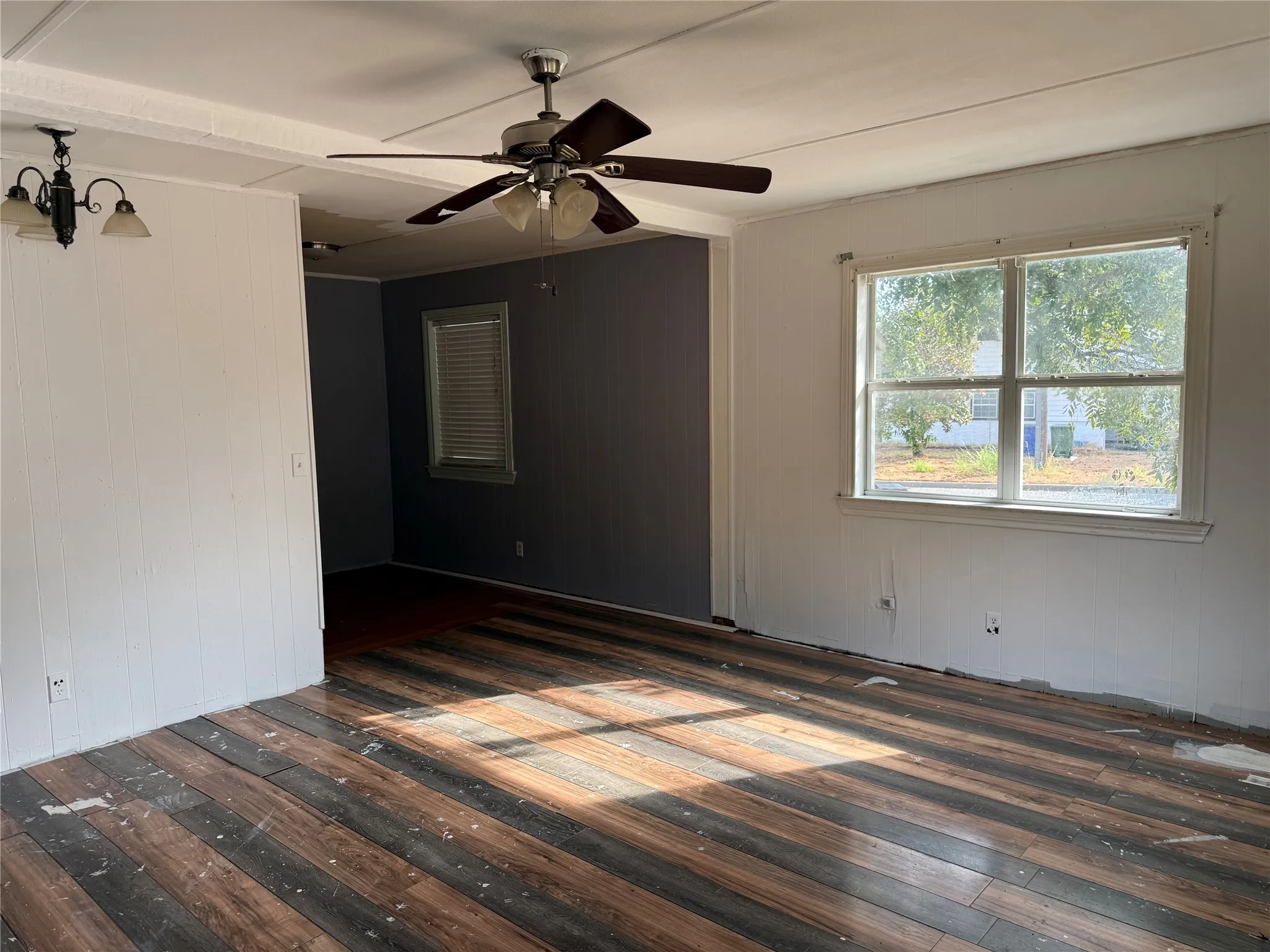 Wood-finish flooring, ceiling fan, natural light from a large window, recessed lighting, and a hanging light fixture