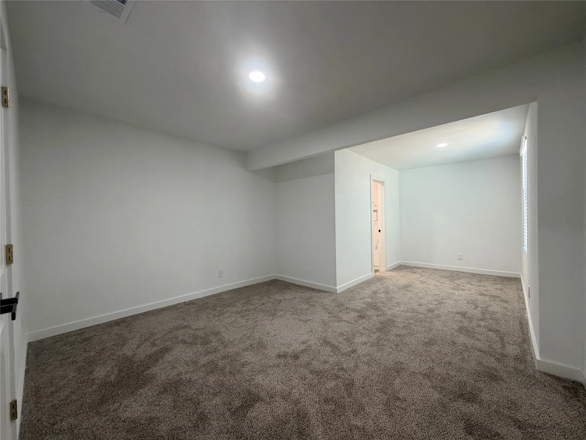 Recessed lighting illuminates the carpeted flooring and white painted walls