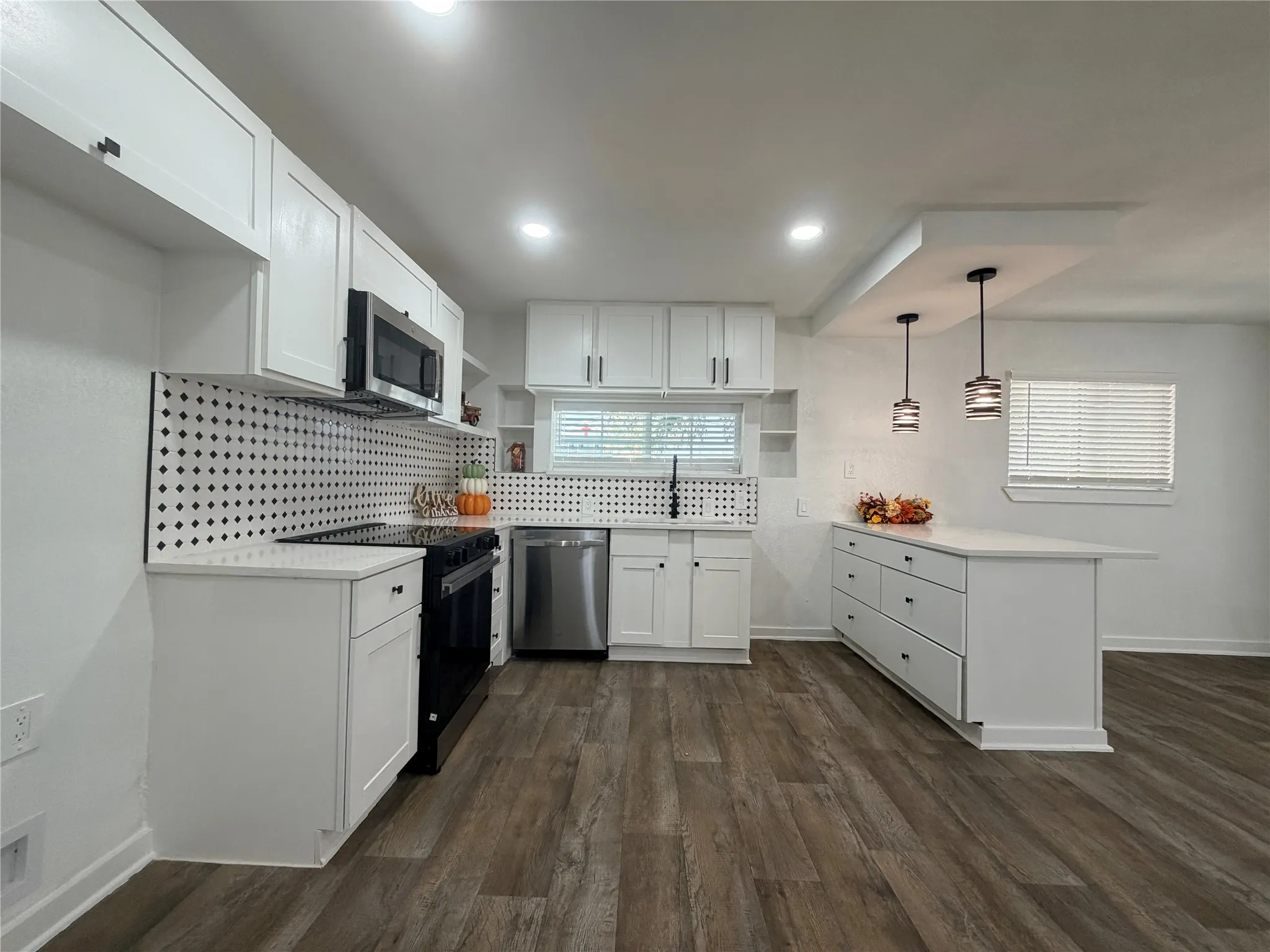 Kitchen featuring white cabinetry, wood-finish flooring, a patterned backsplash, stainless steel appliances, and a central island with pendant lighting