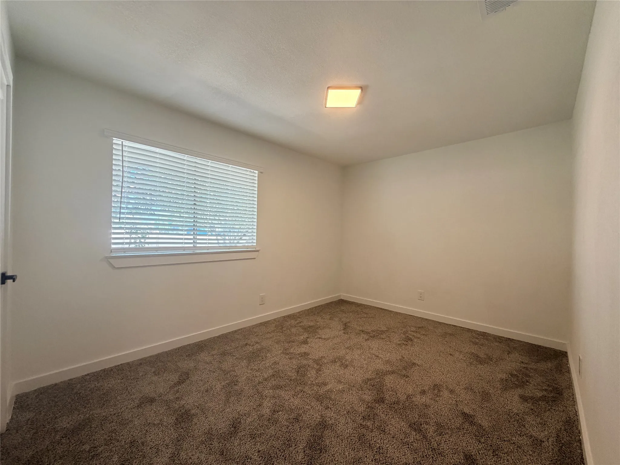 Wall-to-wall carpeting, square ceiling light fixture, white interior walls, and a window with blinds