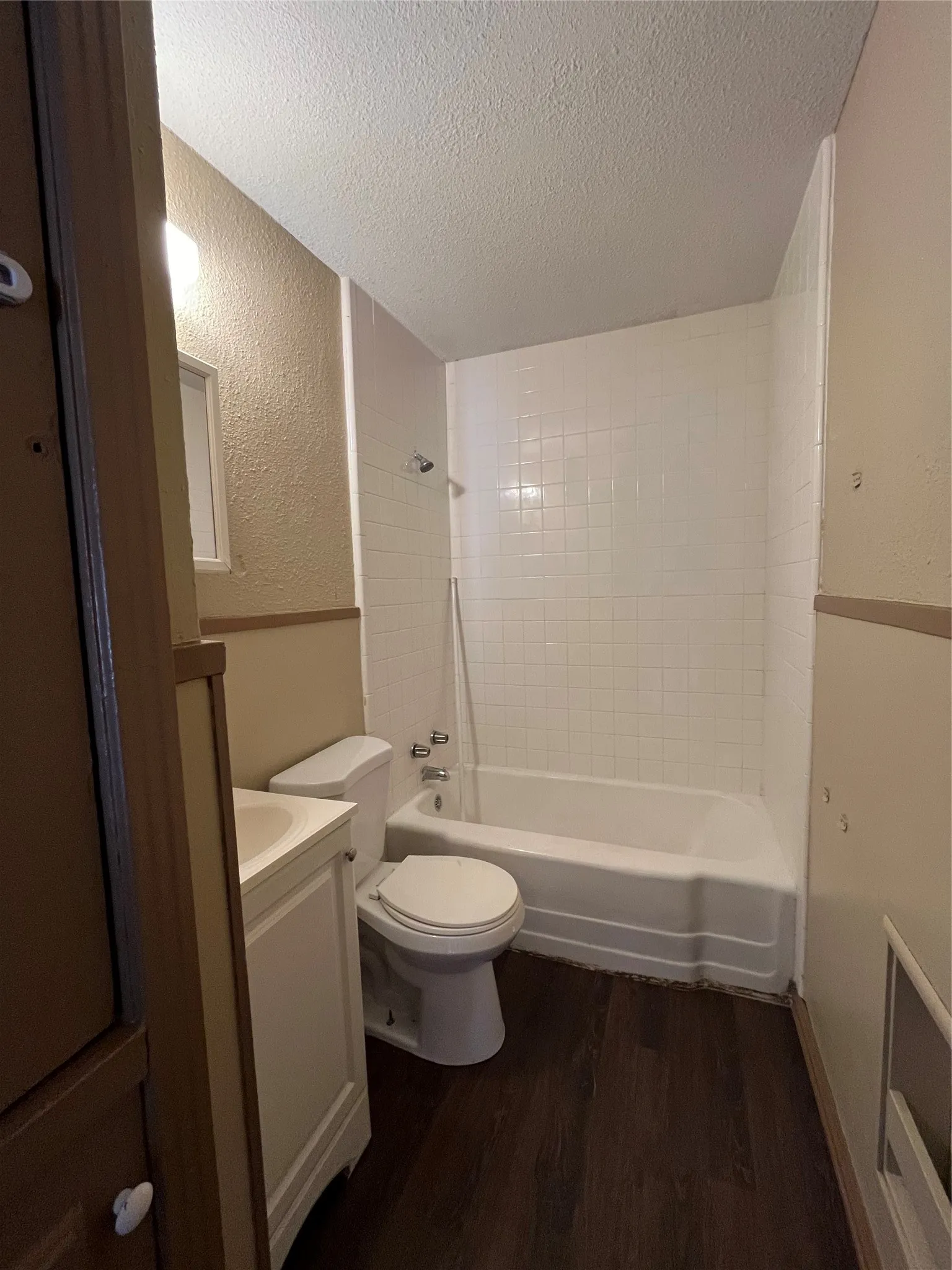 Full bathroom with a textured ceiling, toilet, tiled shower / bath combo, vanity, and hardwood / wood-style flooring