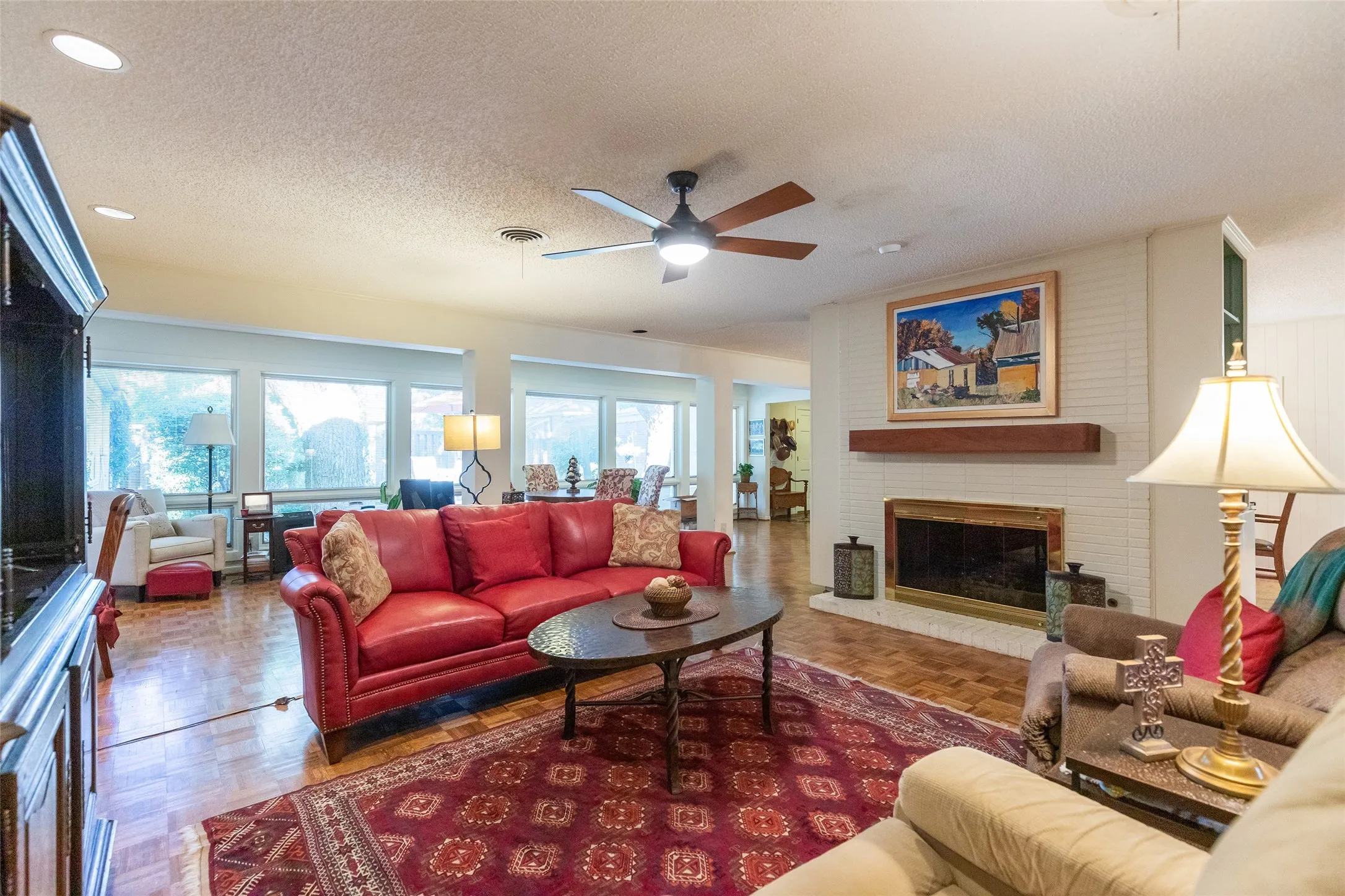 Recessed lighting, wood-finish flooring, white brick fireplace, wood mantel, and large window array