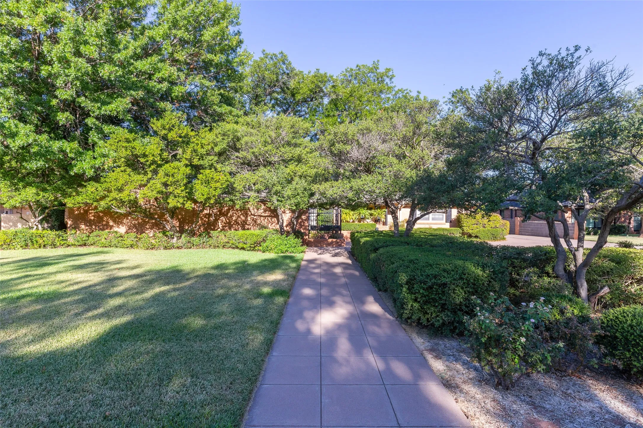 Stone paver walkway flanked by manicured hedges and mature trees
